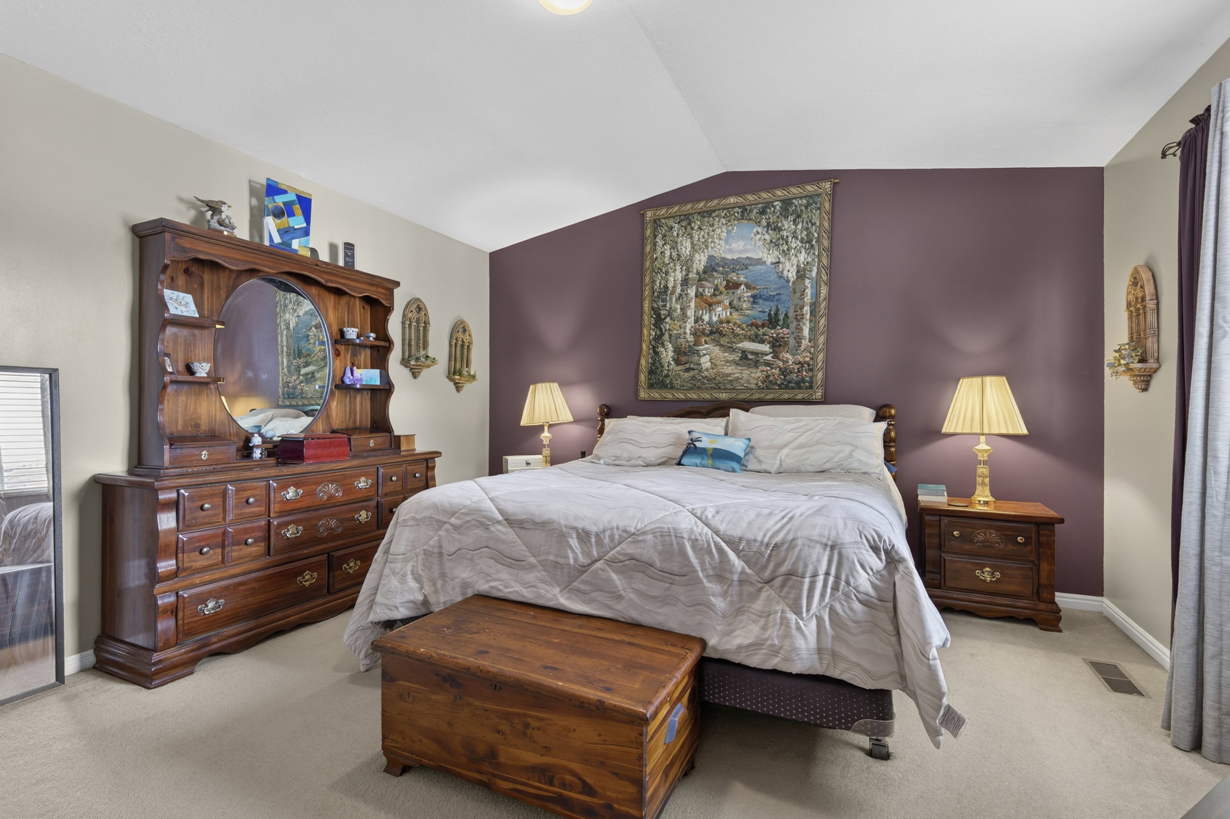 Spacious bedroom featuring vaulted ceilings, plush carpet flooring, and a wall with an accent color