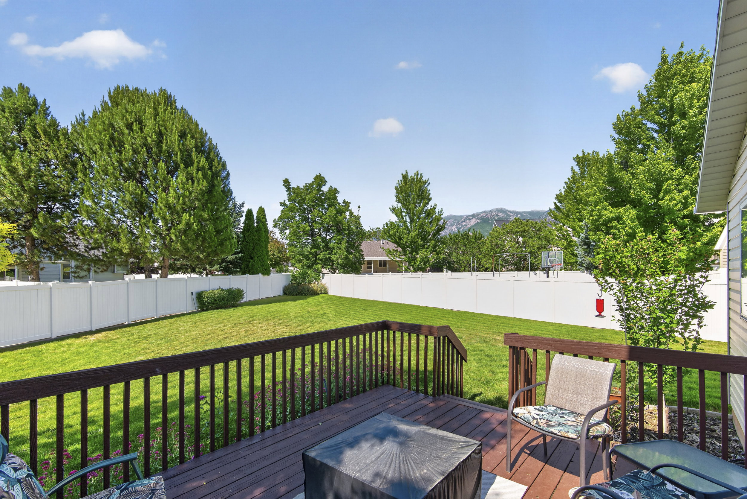 Spacious backyard featuring a wood-finish deck with railings, an expansive manicured lawn, and mature perimeter trees