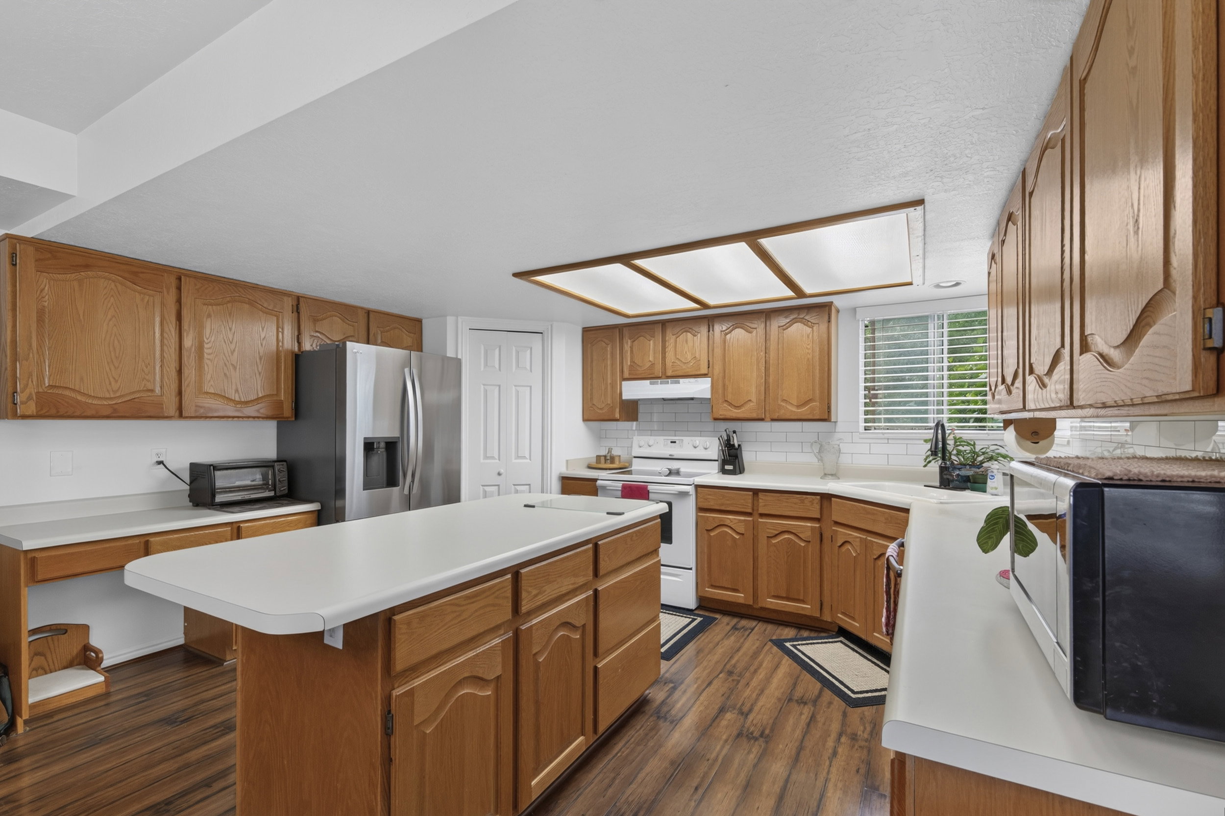 Kitchen featuring wood-finish flooring, wood cabinetry, white countertops, and a subway tile backsplash