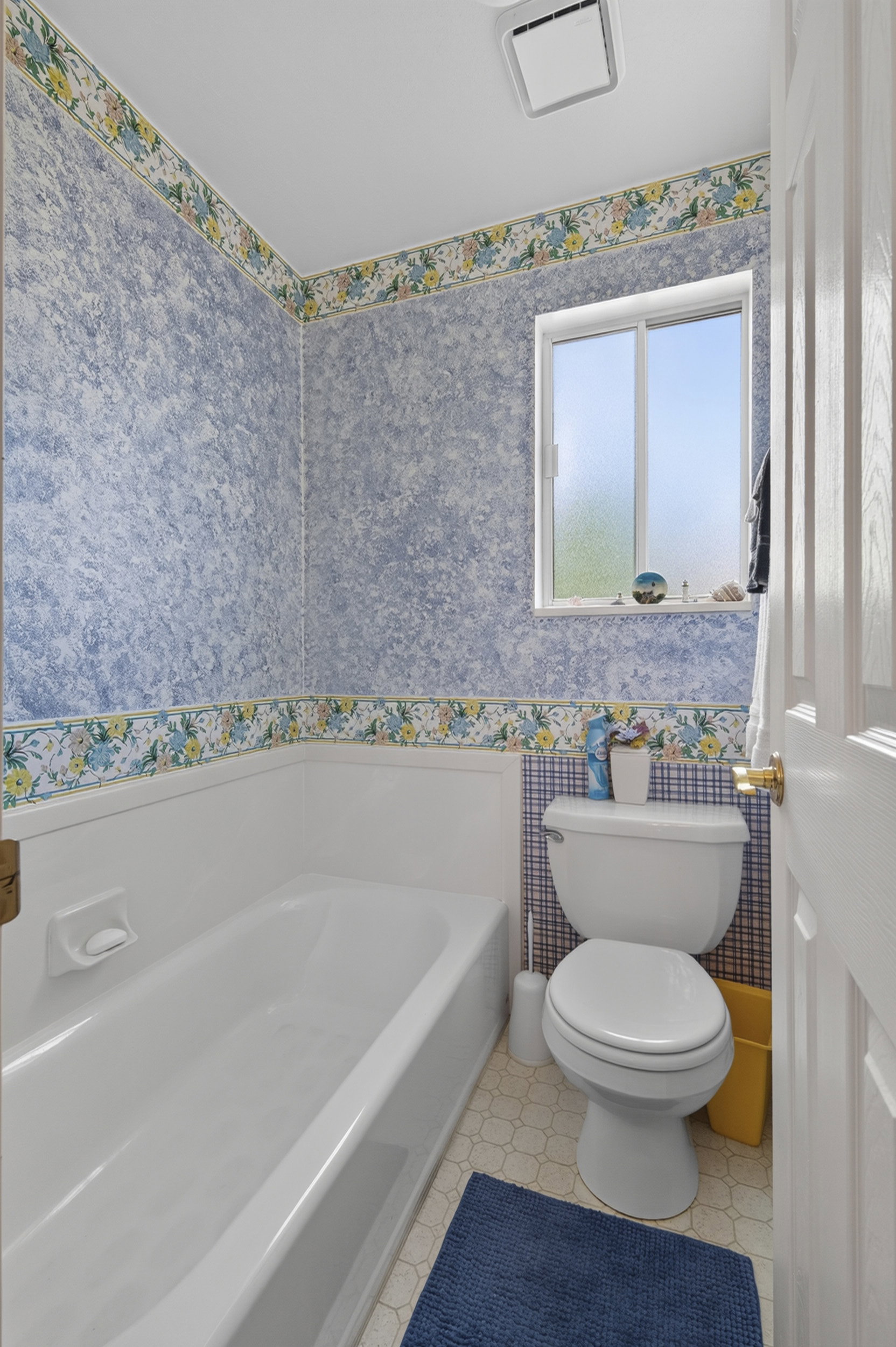 Bathroom featuring a white bathtub, toilet, and a window for natural light