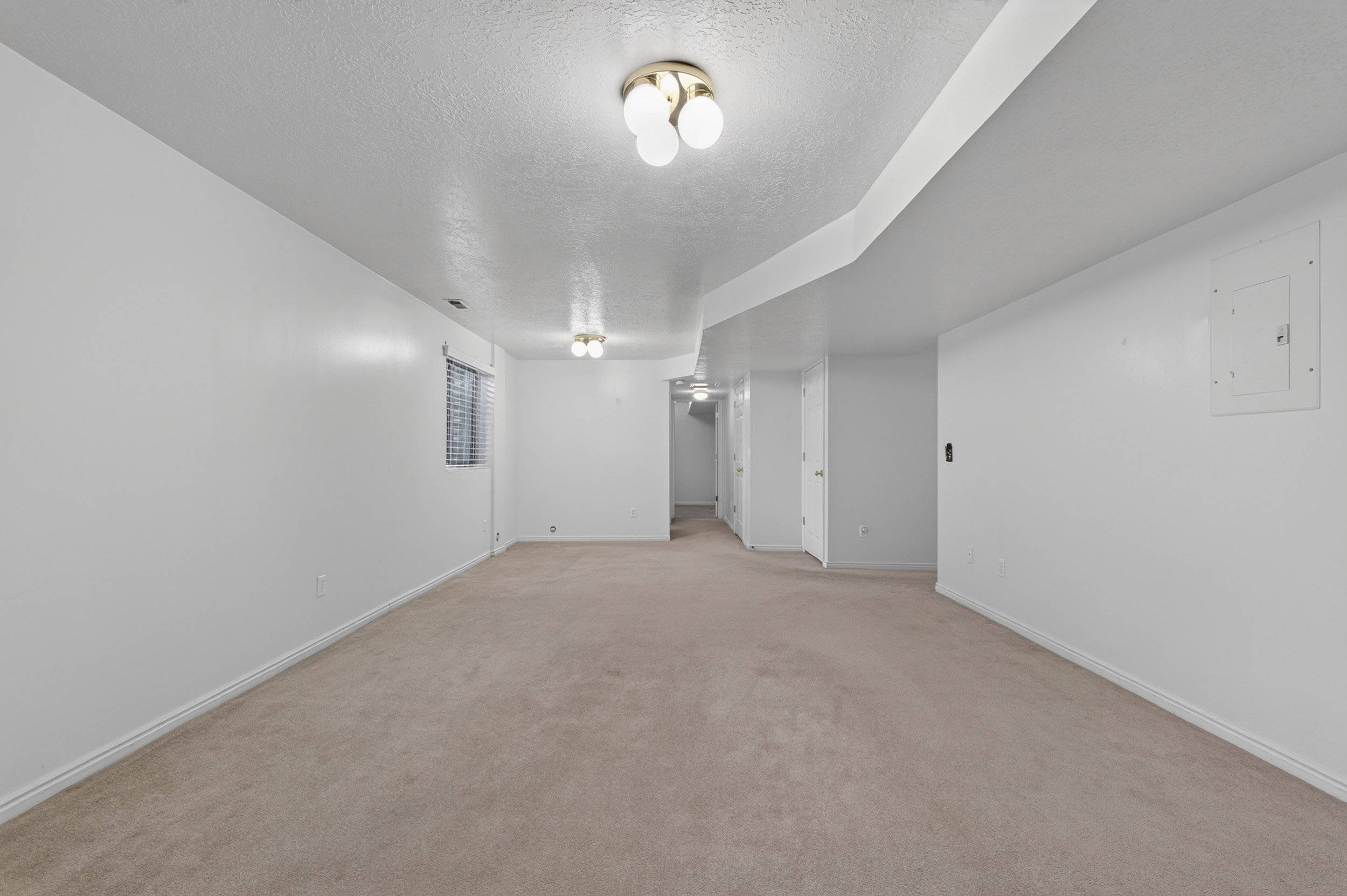 Spacious room featuring neutral carpeting, white painted walls, a window with horizontal blinds, and ceiling-mounted light fixtures