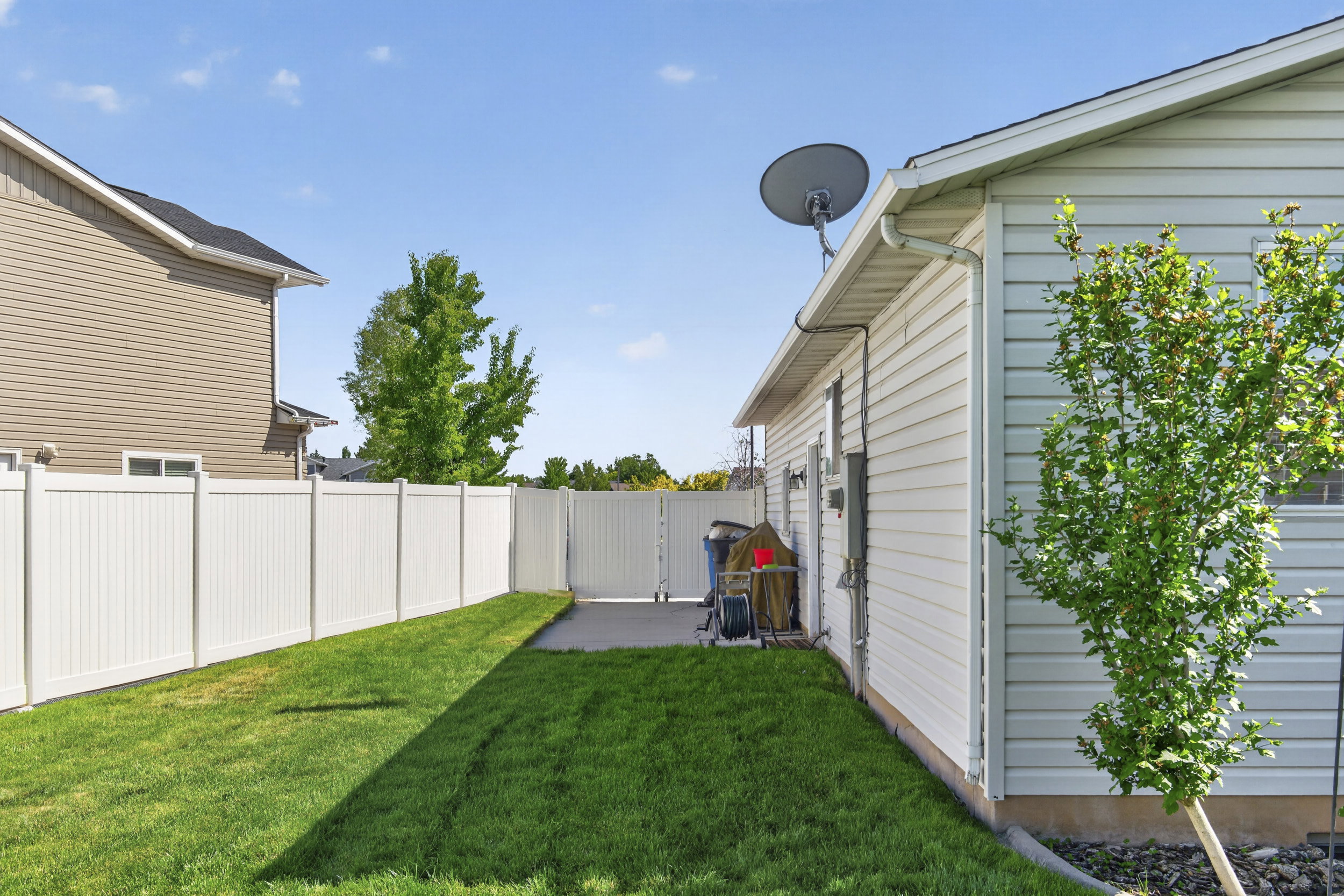 Expansive green lawn featuring a white vinyl fence, concrete patio, and mature landscaping
