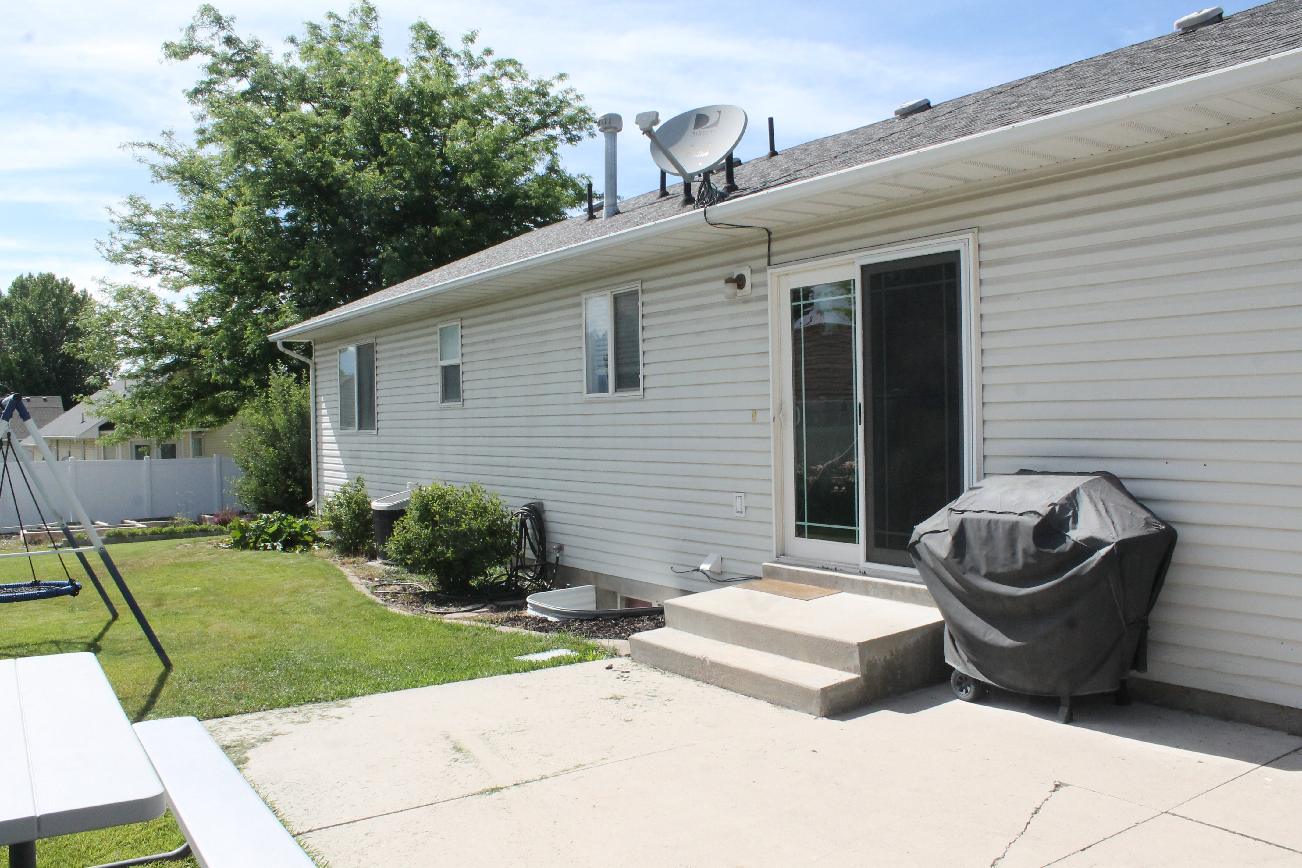 Rear exterior featuring light-colored siding, a concrete patio, and a sliding glass door