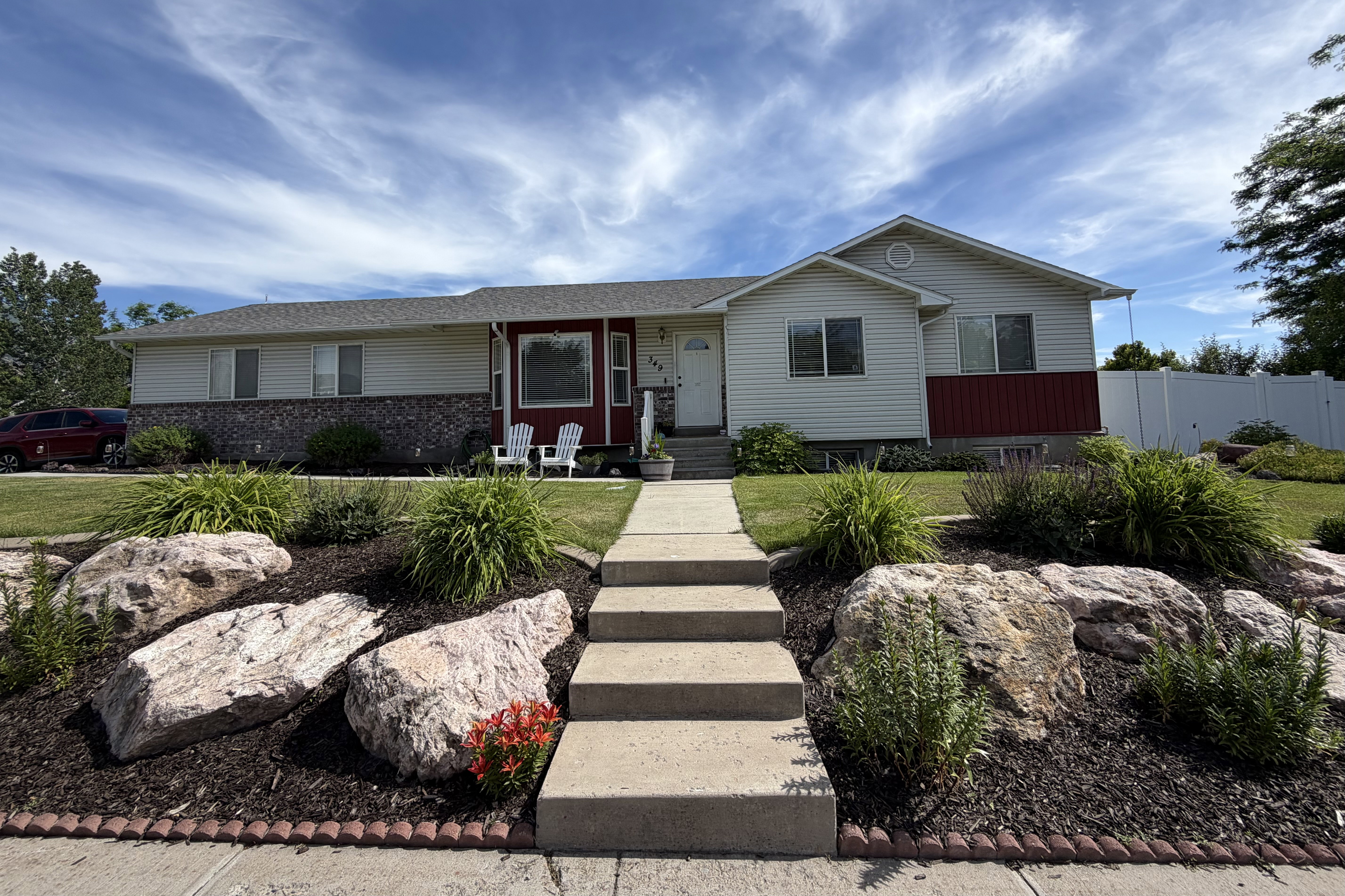 Ranch-style exterior with a split-level entry, red and stone facade accents, concrete walkway, and landscaped rock garden