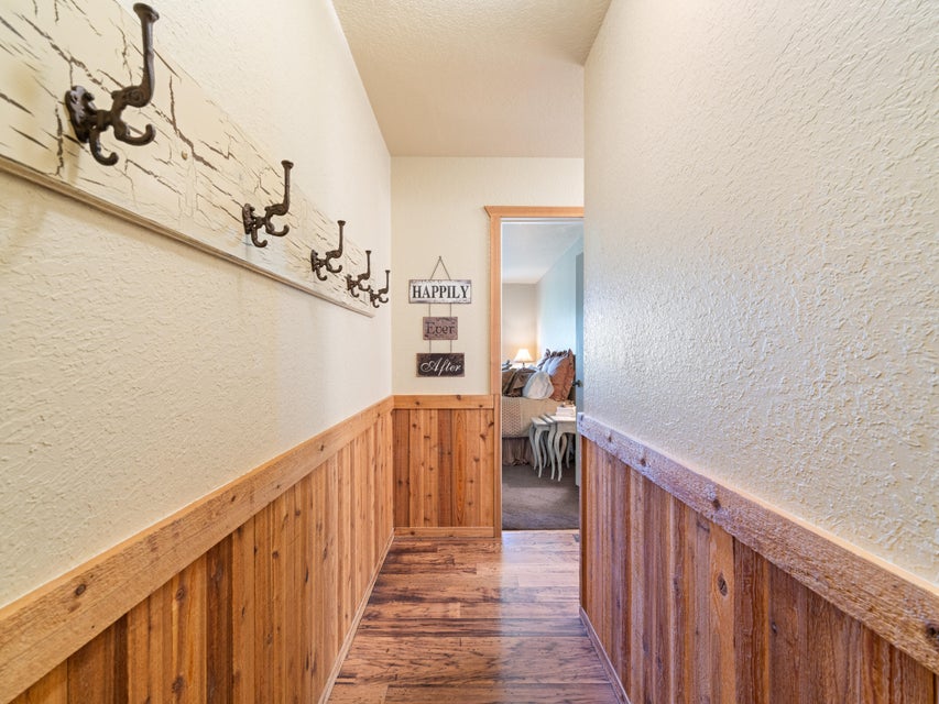 Hallway featuring wood-finish flooring, half-wall wood paneling, and a mounted coat rack with multiple hooks
