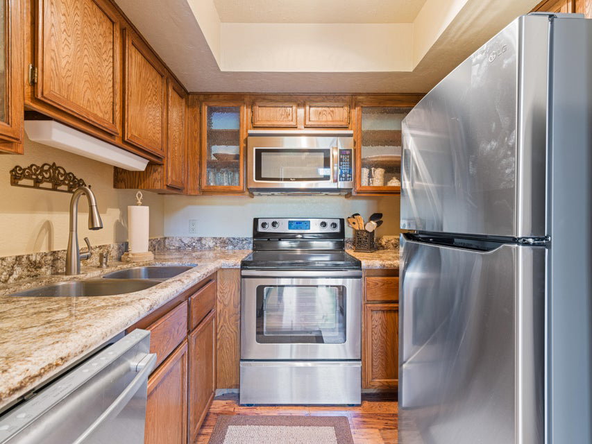 Kitchen featuring wood cabinetry, stainless steel appliances, a double basin sink with a gooseneck faucet, and stone countertops