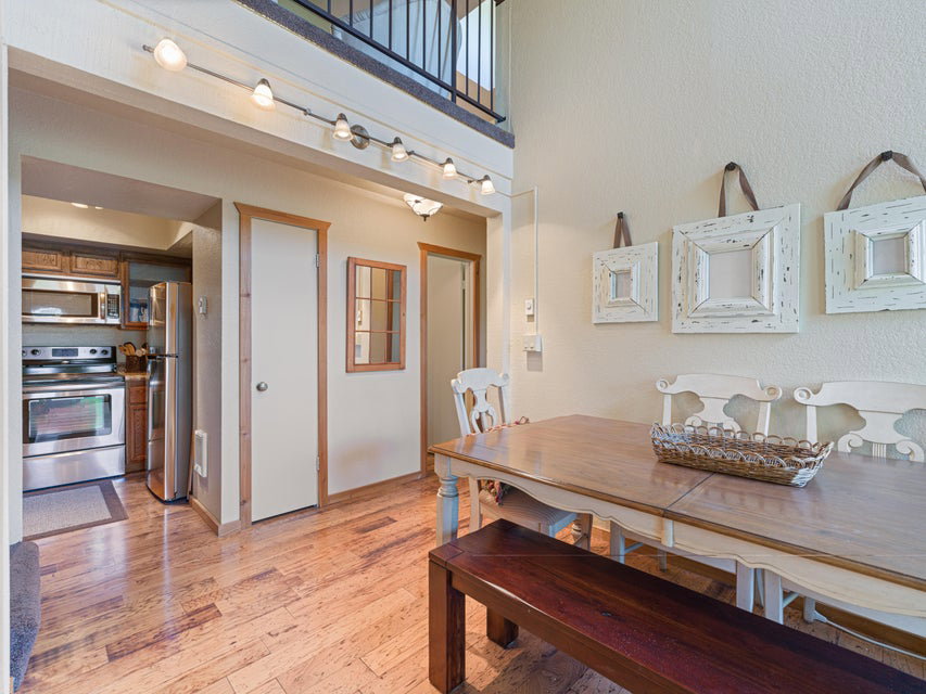 Dining area featuring wood-finish flooring, a kitchen pass-through, track lighting, and a loft overlook with a black metal railing
