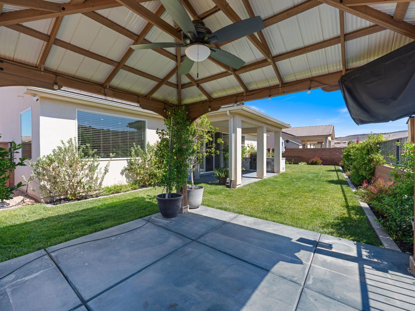 Expansive concrete patio beneath a pergola featuring a ceiling fan and string lighting