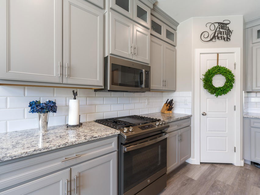Kitchen featuring light gray cabinetry, stainless steel appliances, speckled stone countertops, and white subway tile backsplash