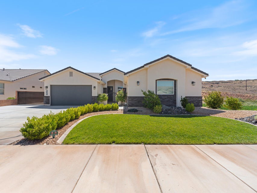 Single-story residence featuring a cream stucco facade with dark stone accents, a dark asphalt shingle roof, and an attached two-car garage