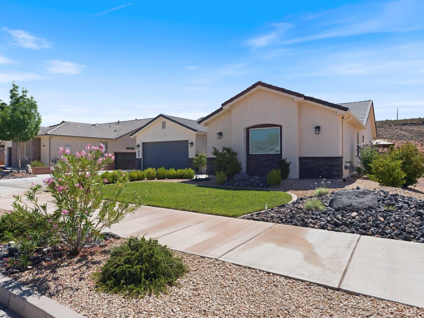 Contemporary stucco exterior with a stone veneer accent, featuring a low-pitched tile roof, landscaped front yard with lush green lawn, and a concrete driveway