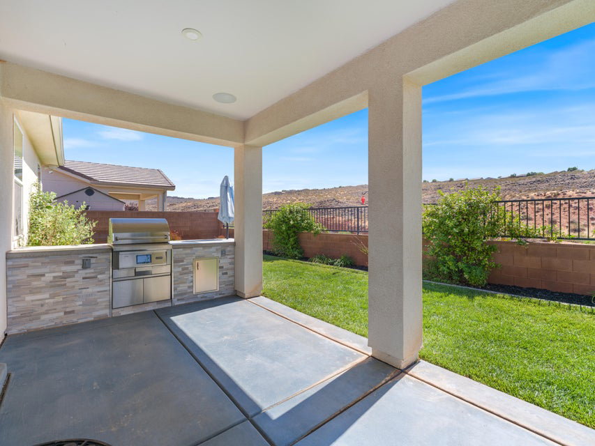 Covered patio featuring an outdoor kitchen with stainless steel grill, stone veneer accent wall, and built-in storage