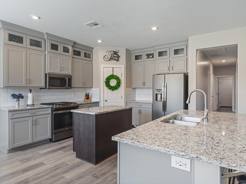 Modern kitchen featuring light gray cabinetry with upper glass-front accents, stainless steel appliances, and granite countertops