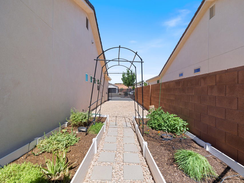 Landscaped side yard featuring a decorative metal archway, a gravel path with stepping stones, and raised garden beds