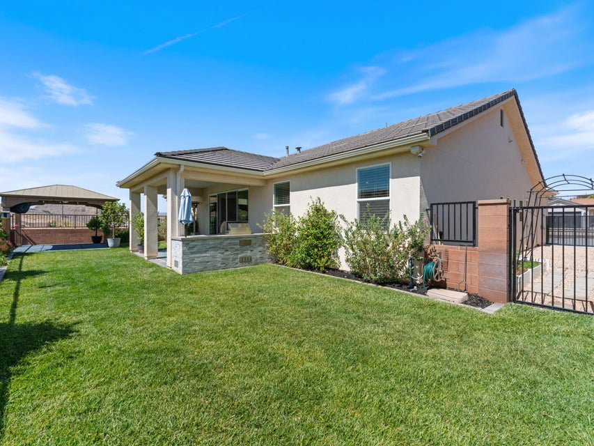 Expansive backyard featuring a covered patio with columns, a stone veneer retaining wall, a manicured lawn, and a fenced area with an arched gate