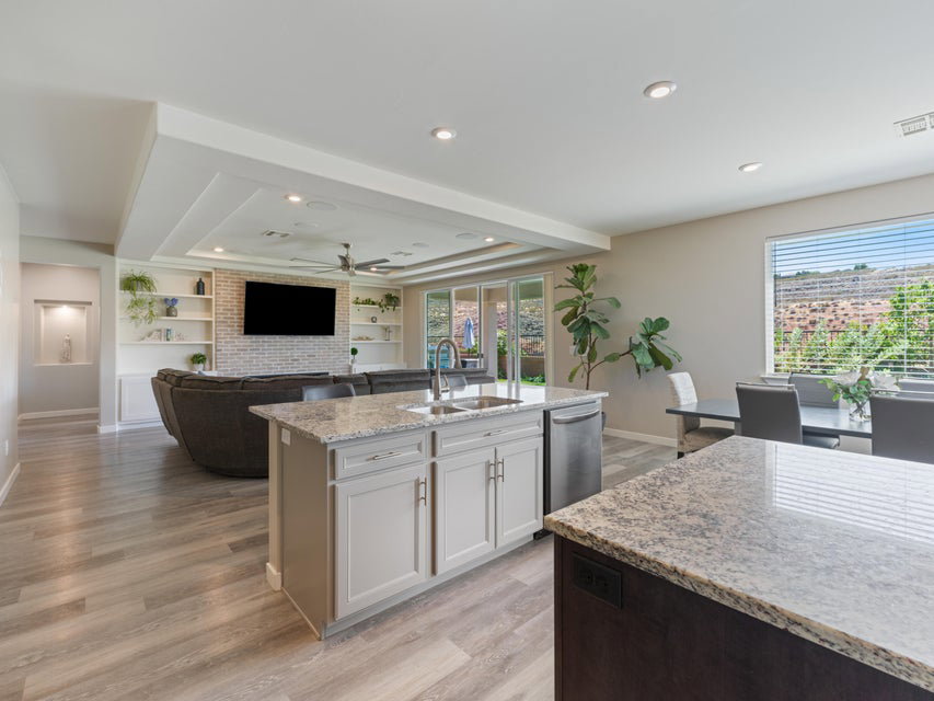 Open-concept living area featuring wood-finish flooring, a kitchen island with stone countertops and an integrated sink, and an exposed brick accent wall