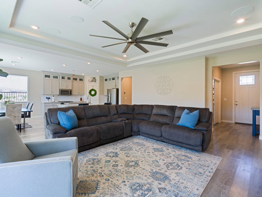 Expansive living area featuring tray ceilings, recessed lighting, a modern ceiling fan, wood-finish flooring, and direct access to the kitchen
