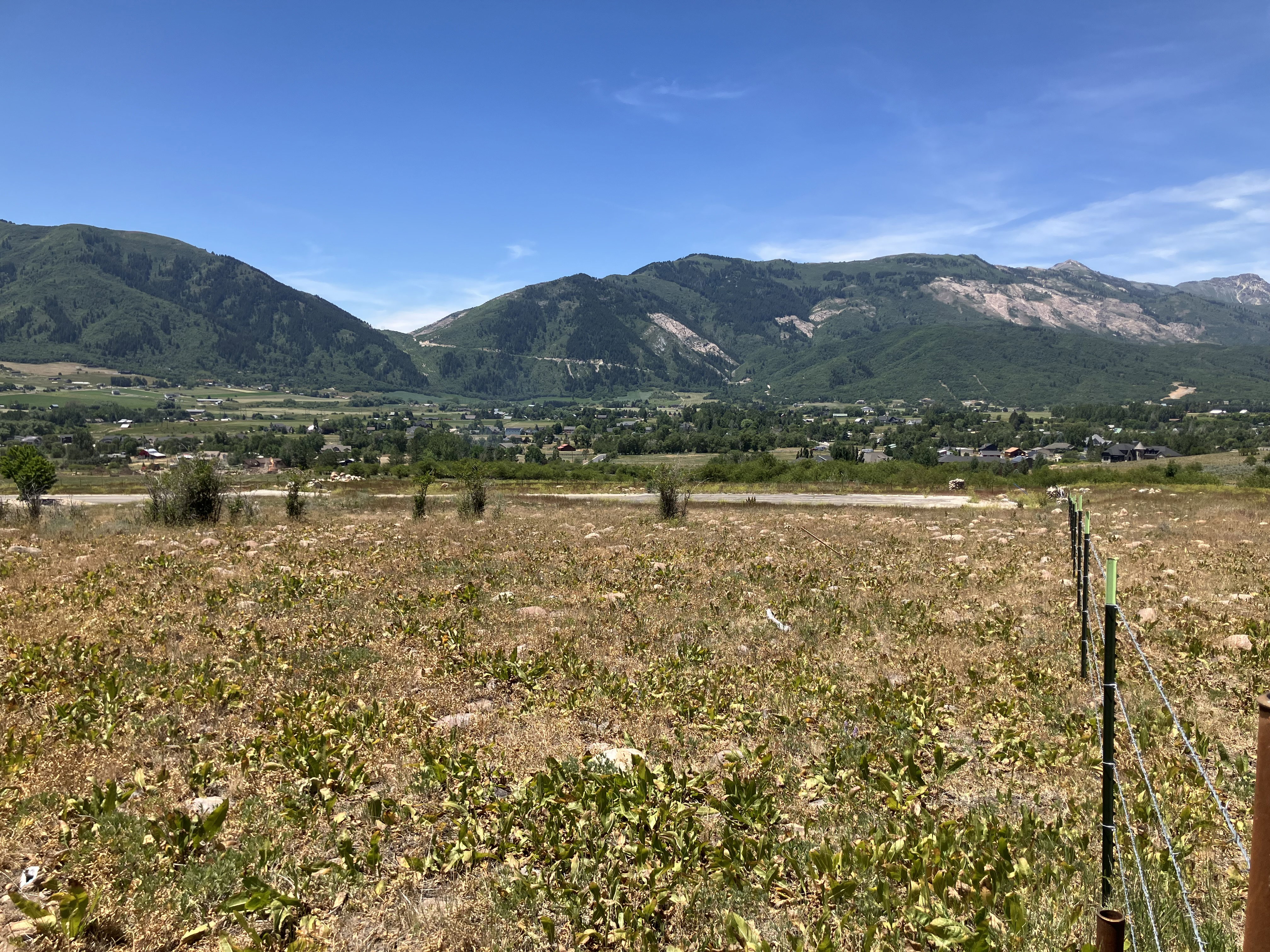 Expansive undeveloped land featuring a partial wire fence and distant mountainous terrain