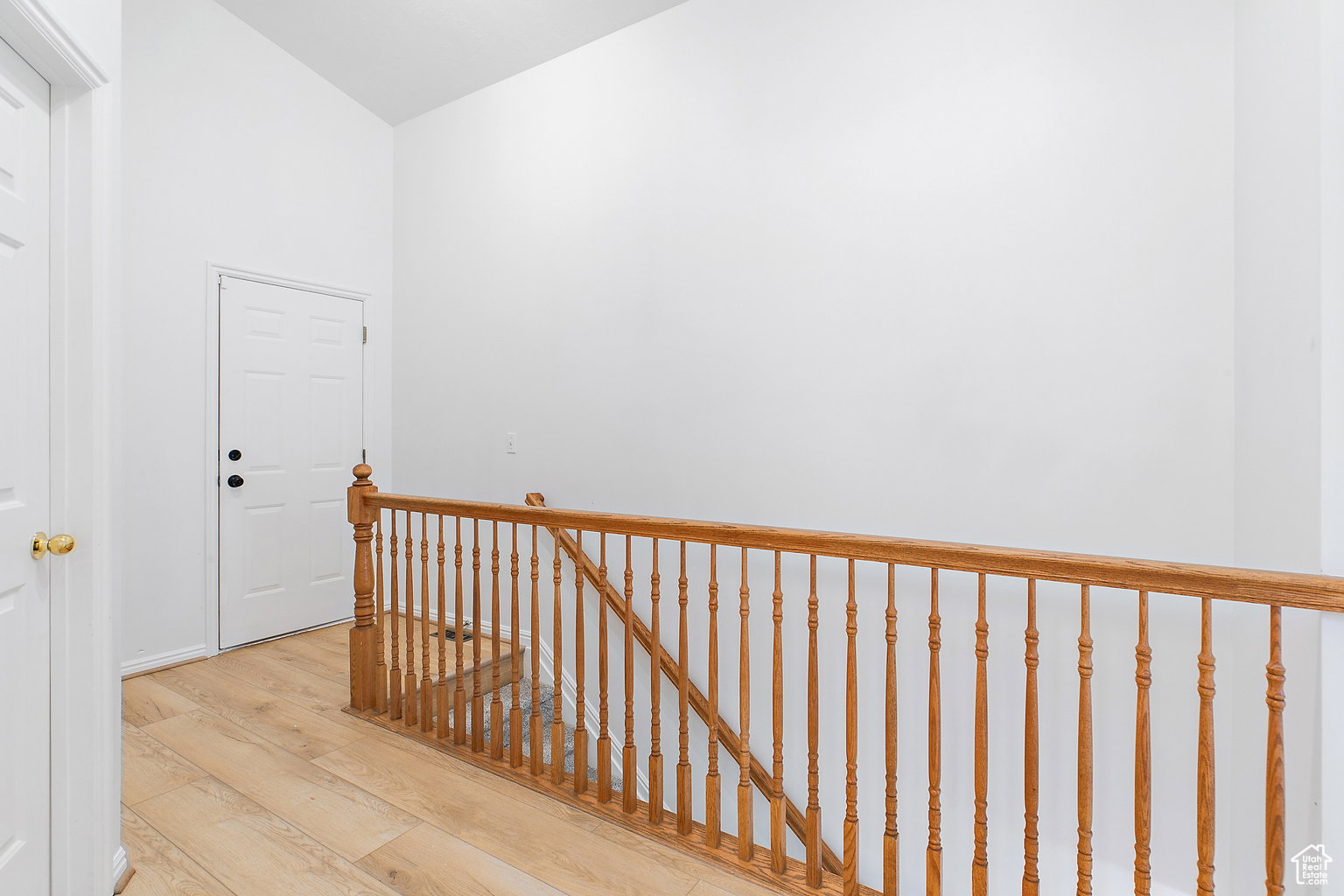 Upper level landing featuring wood-finish flooring, a white paneled door, and a wooden railing with turned balusters