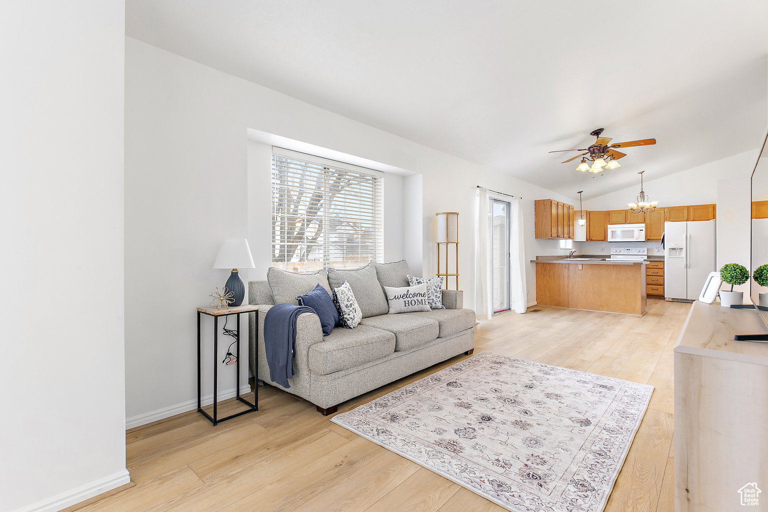 Bright open-concept living space featuring wood-finish flooring, white walls, and a large window with blinds