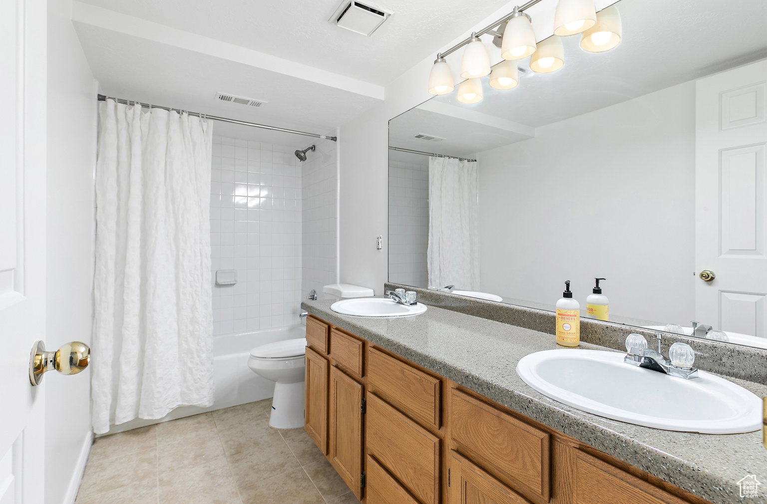 Bathroom featuring a double vanity with light wood cabinetry and a speckled countertop