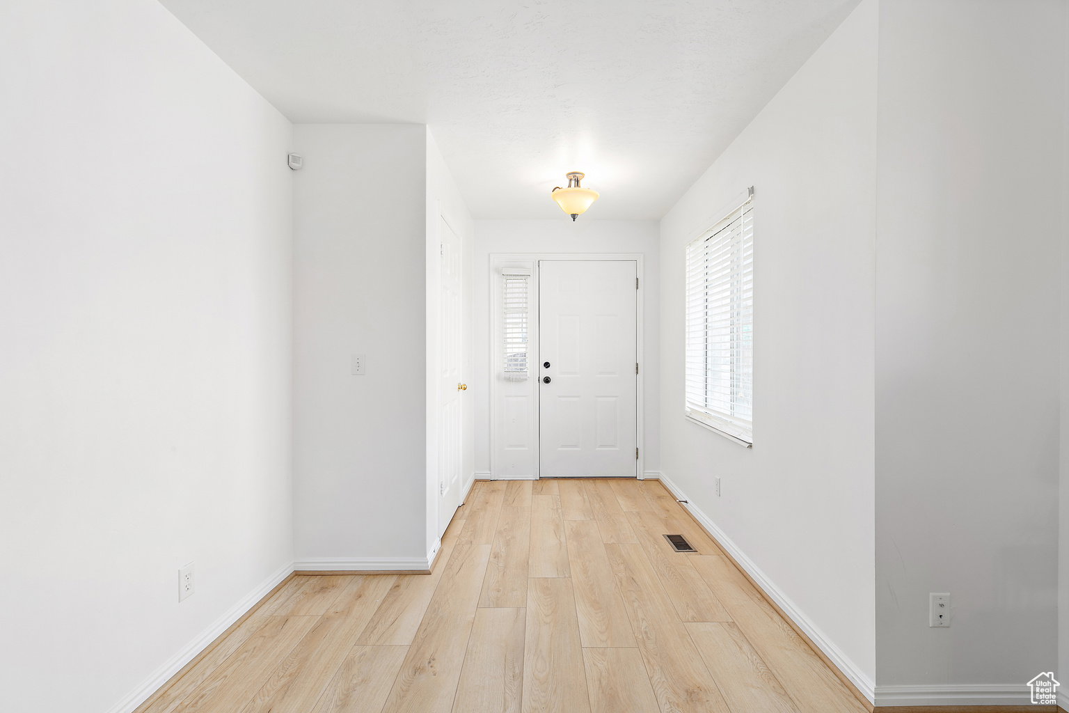 Entryway featuring a paneled door, wood-finish flooring, white baseboards, and a window with blinds