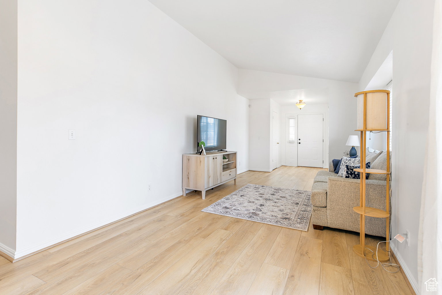 Living area featuring wood-finish flooring, vaulted ceilings, and a front entry door with a sidelight
