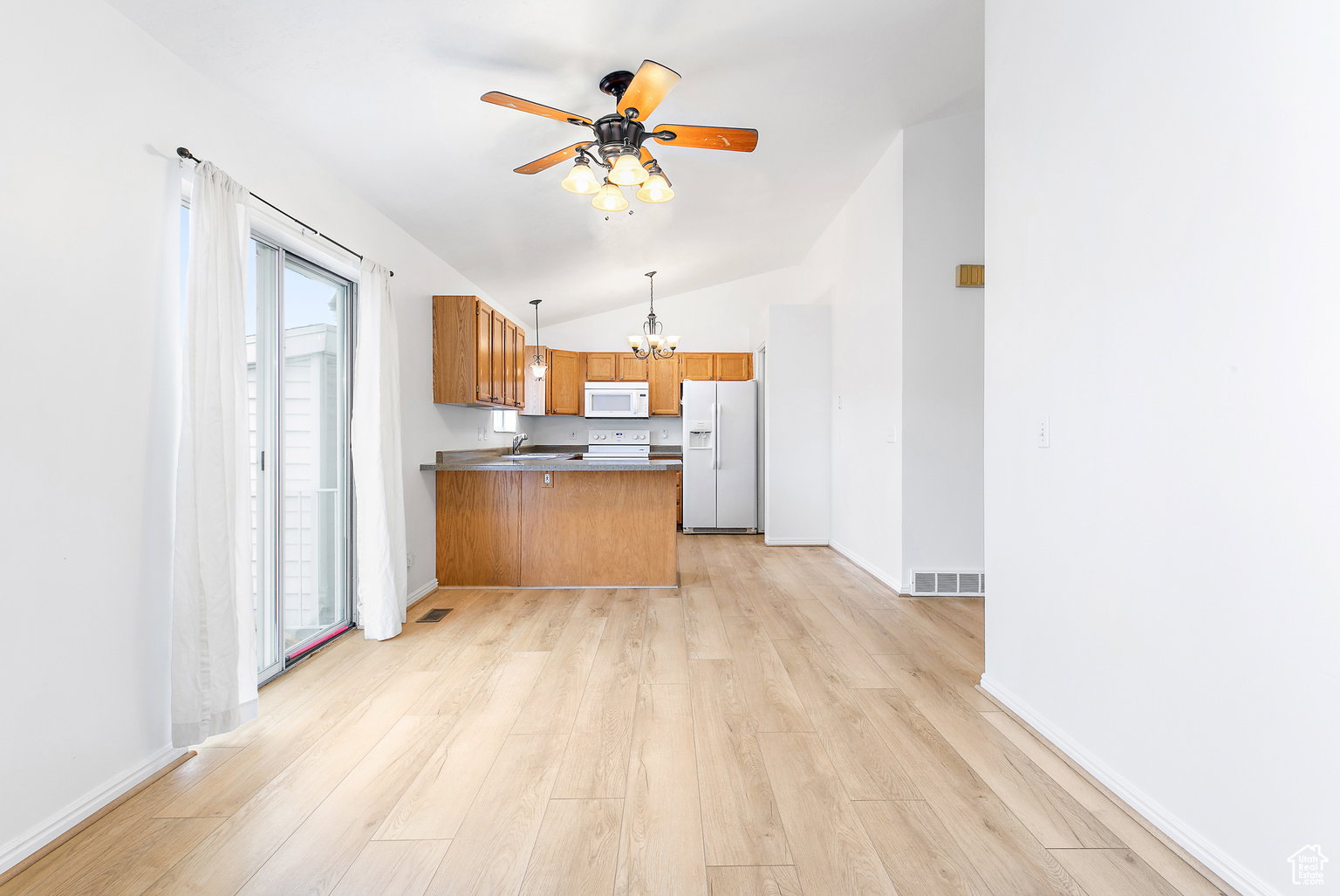 Open-concept living area with light wood-finish flooring, vaulted ceilings, and a ceiling fan with integrated lighting