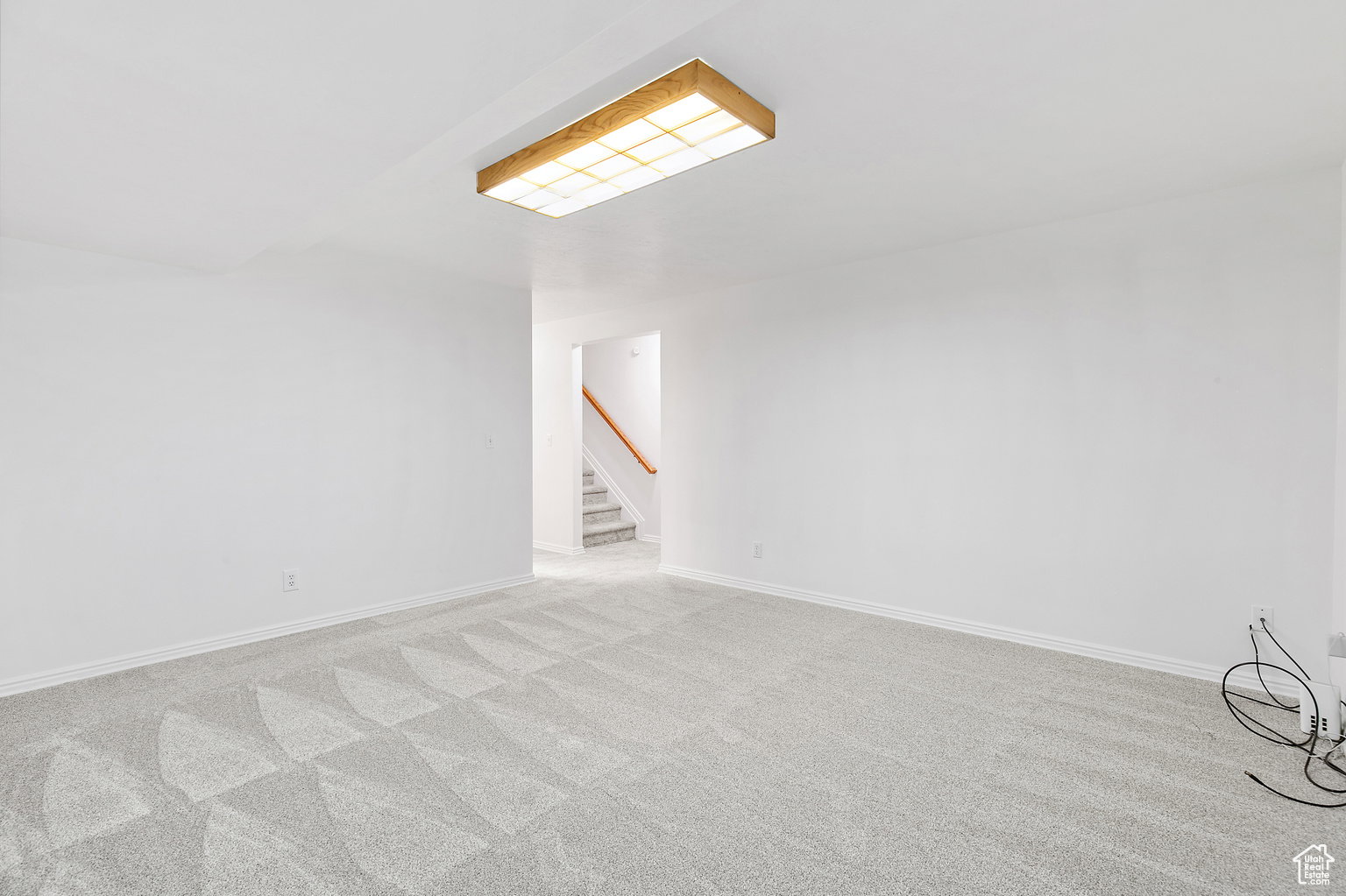 Bright room featuring light gray patterned carpet, white walls, and a wooden flush-mount ceiling light fixture