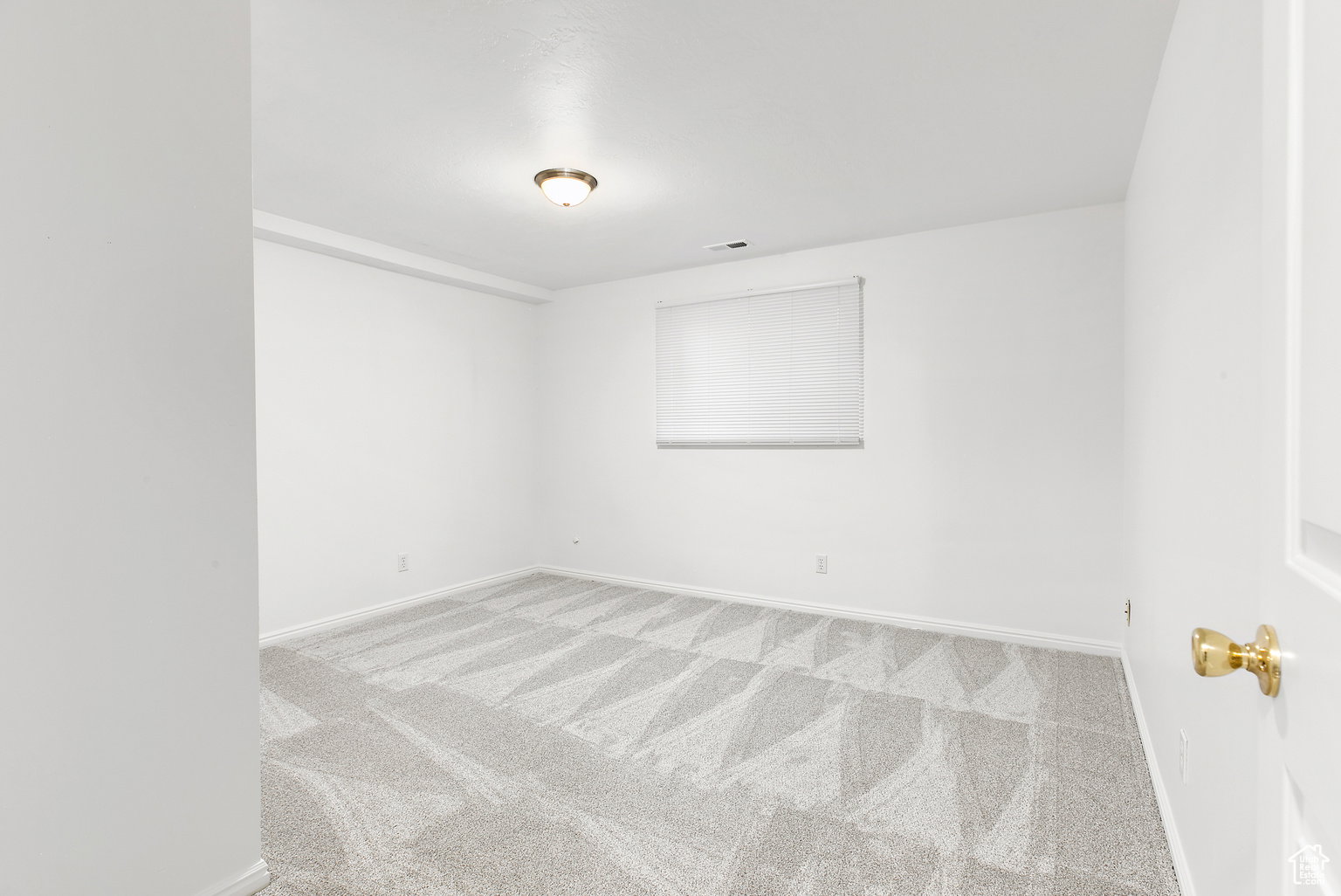 Carpeted room with a window featuring a white roller shade, white walls, and a ceiling-mounted light fixture
