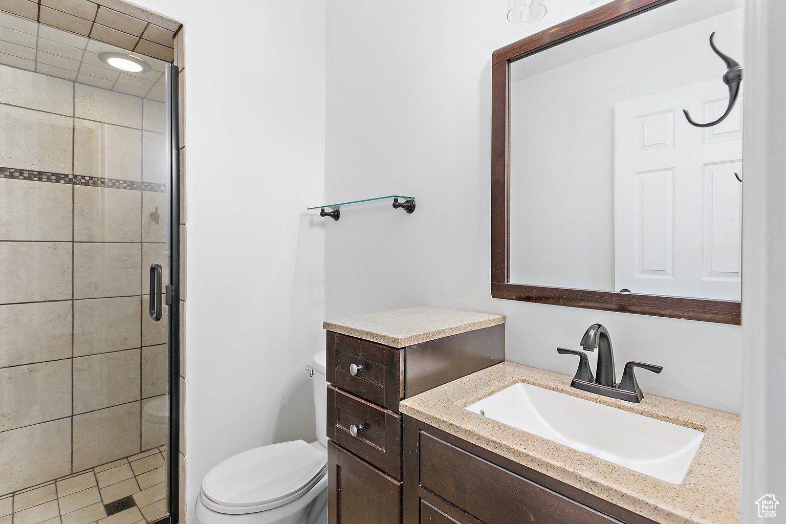 Bathroom featuring a glass-enclosed shower with tiled walls and an accent band, a single vanity with a light-toned countertop, a rectangular undermount sink, and a framed mirror