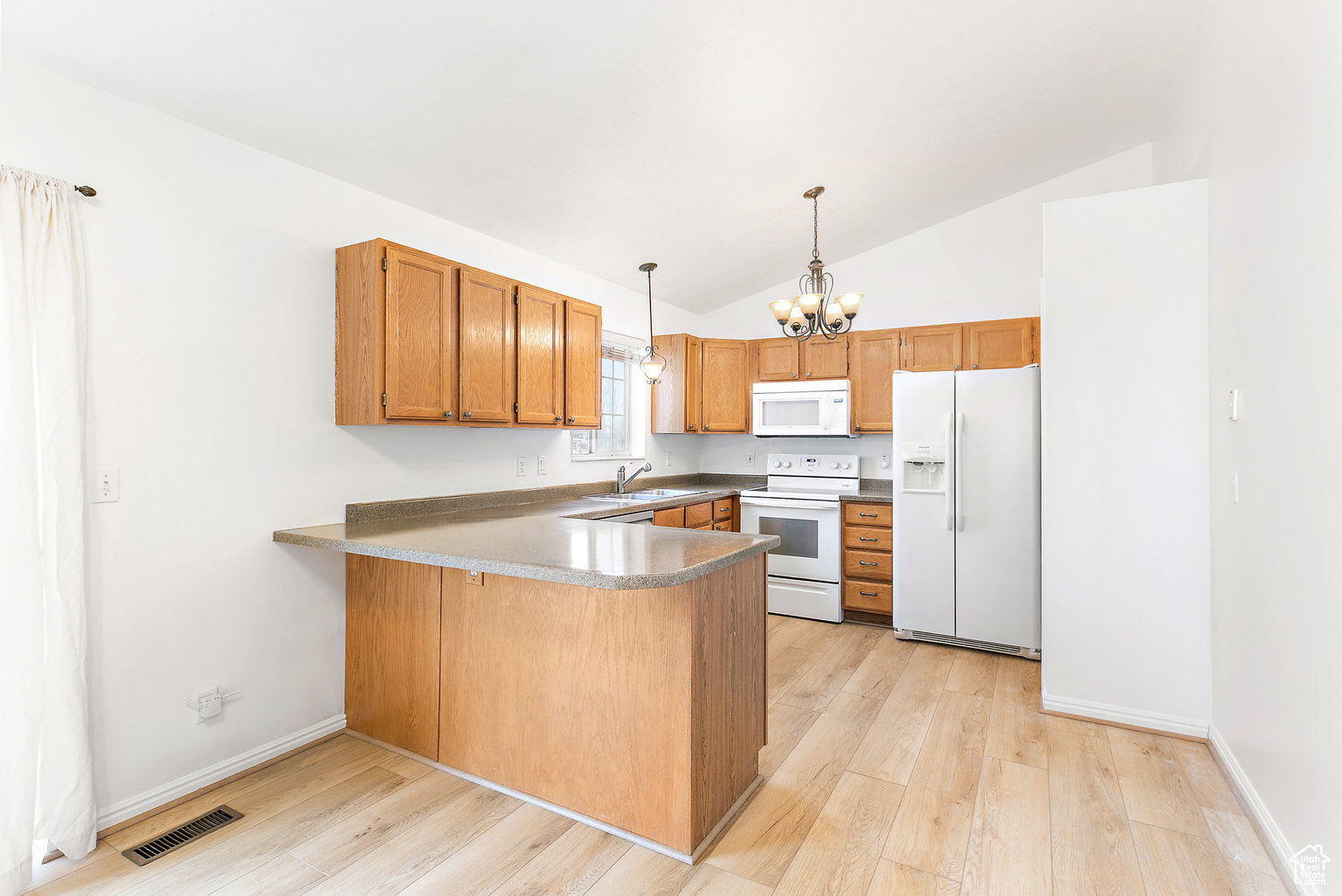 Kitchen featuring wood-finish flooring, light wood cabinetry, white appliances, and a breakfast bar