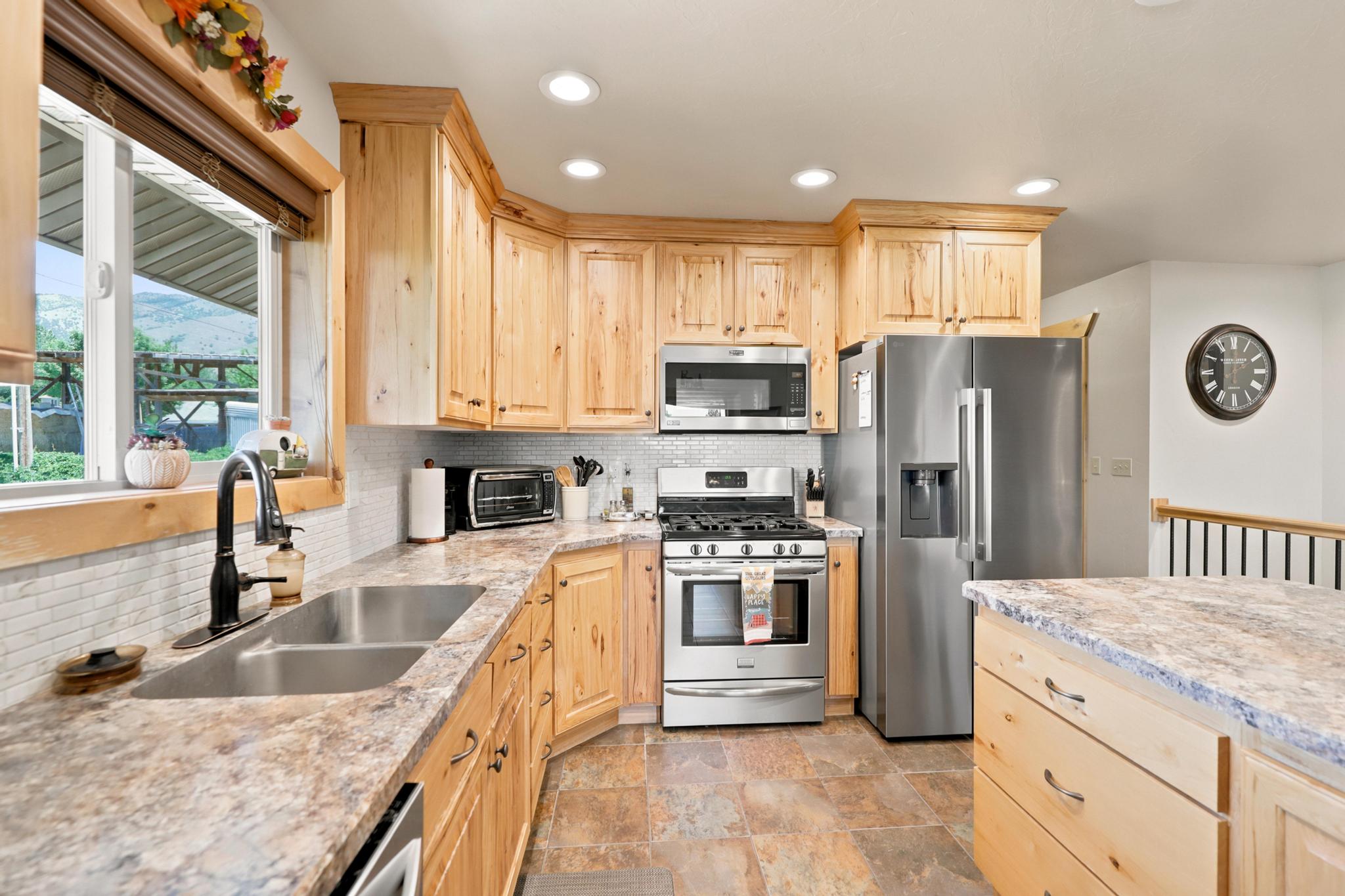 Kitchen featuring light wood cabinetry, stone-look countertops, stainless steel appliances, a double basin sink with a black fixture, and recessed lighting