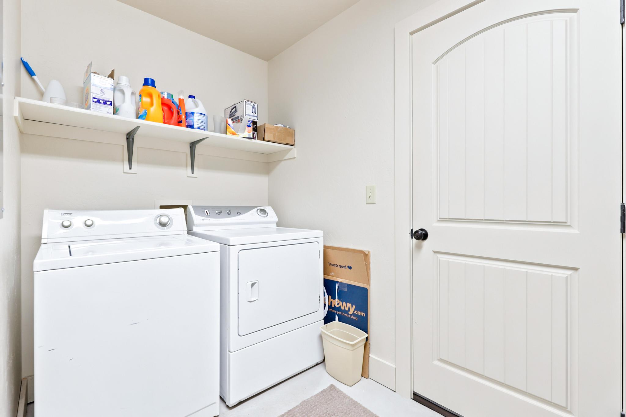 Laundry area featuring a built-in wall shelf, a top-load washer, a front-load dryer, and a paneled interior door with an arched top detail