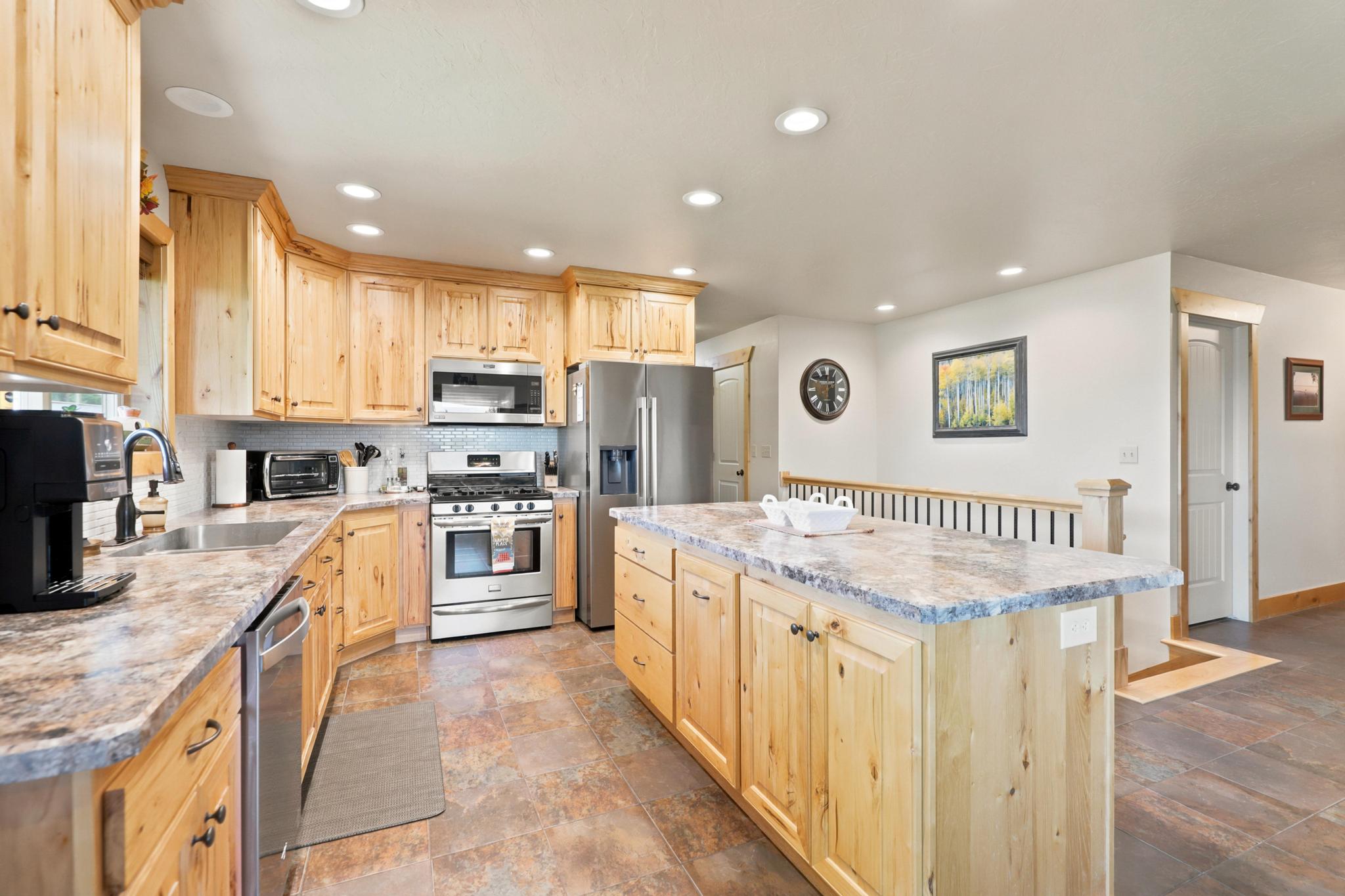 Spacious kitchen featuring light wood cabinetry, stainless steel appliances, a large center island with countertop seating, recessed lighting, and tile flooring