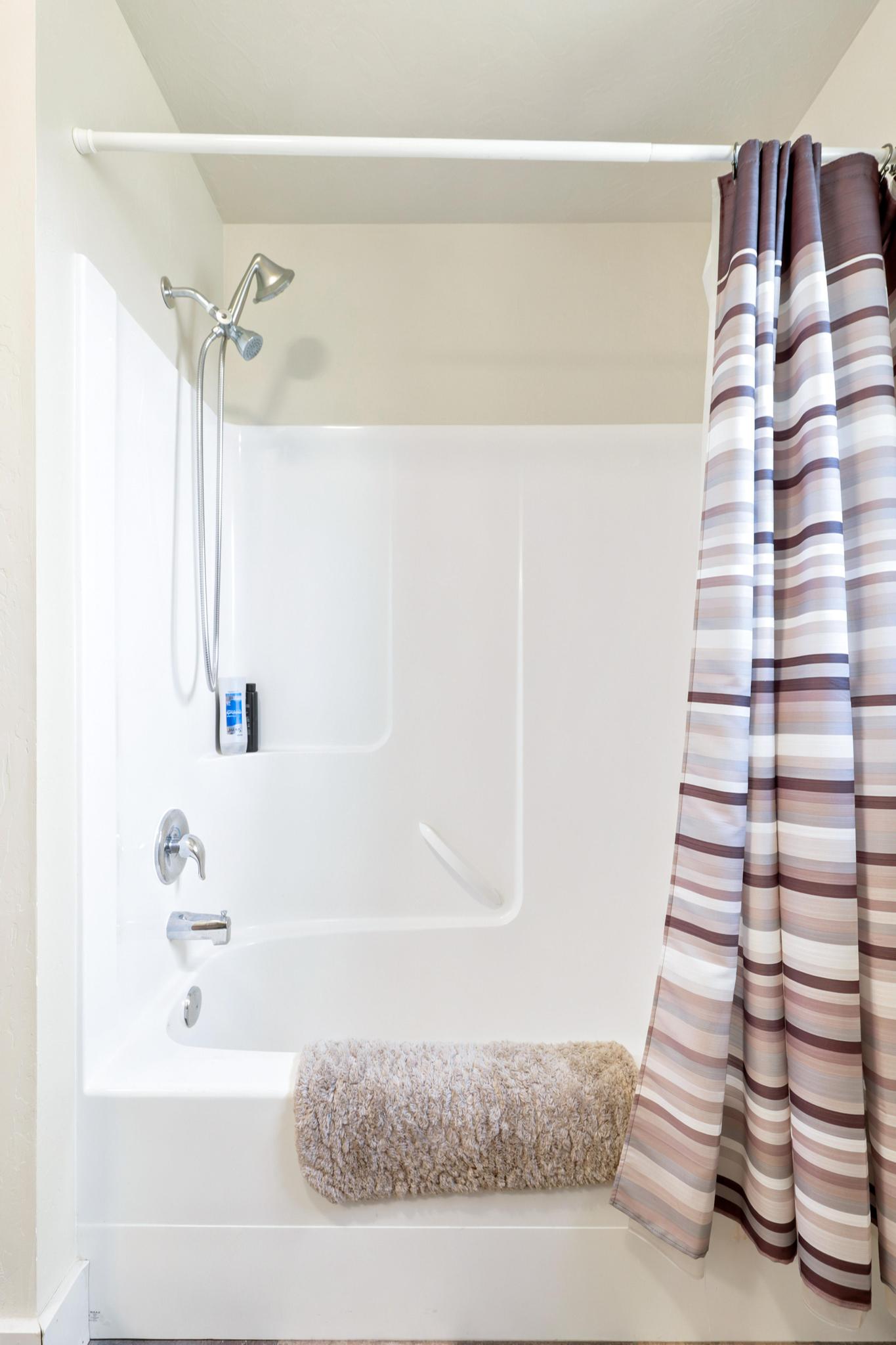 White fiberglass shower and tub combination featuring a chrome showerhead with handheld attachment and coordinating faucet