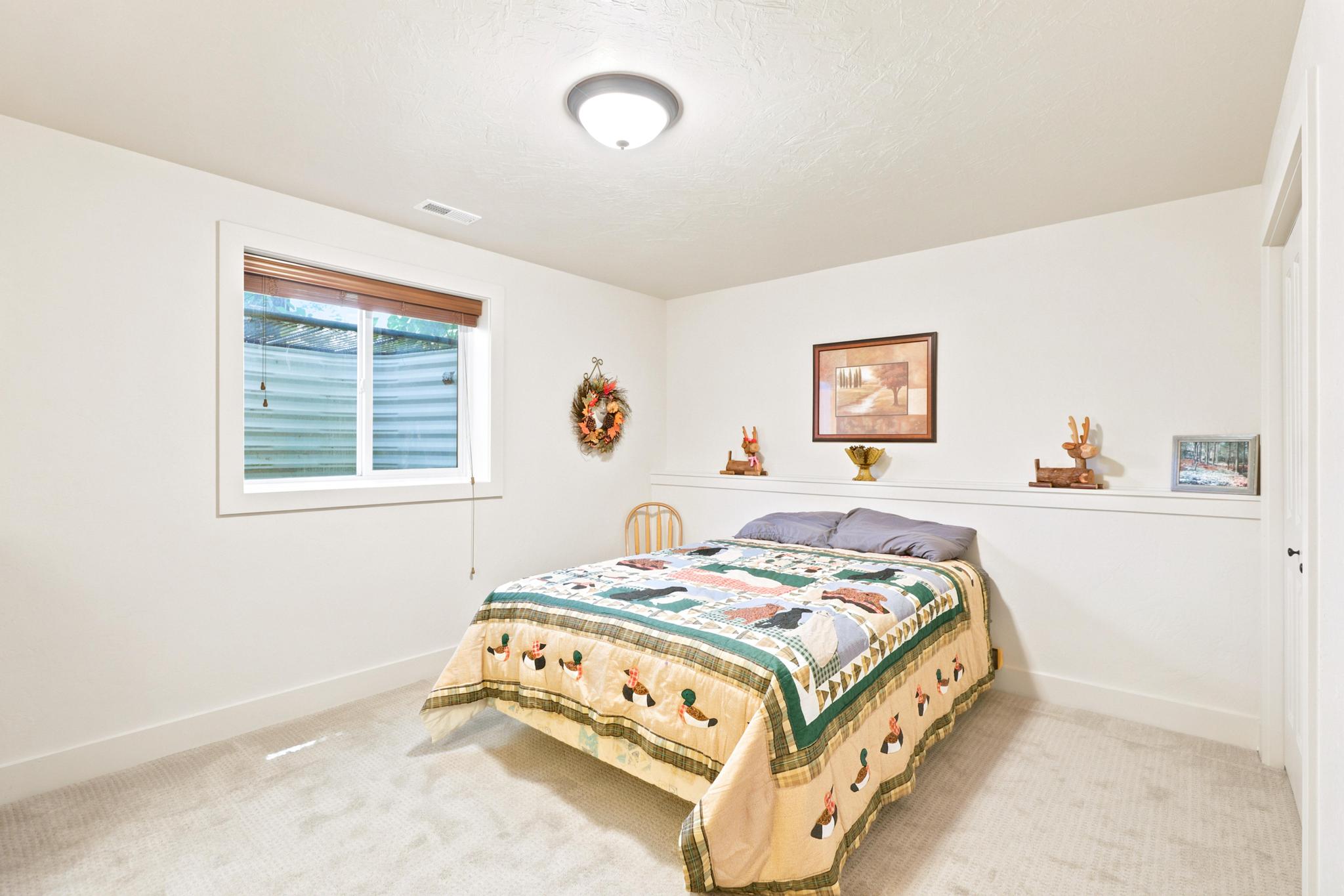 Carpeted bedroom featuring a window with integrated blinds, a wall-mounted display ledge, and a ceiling-mounted light fixture