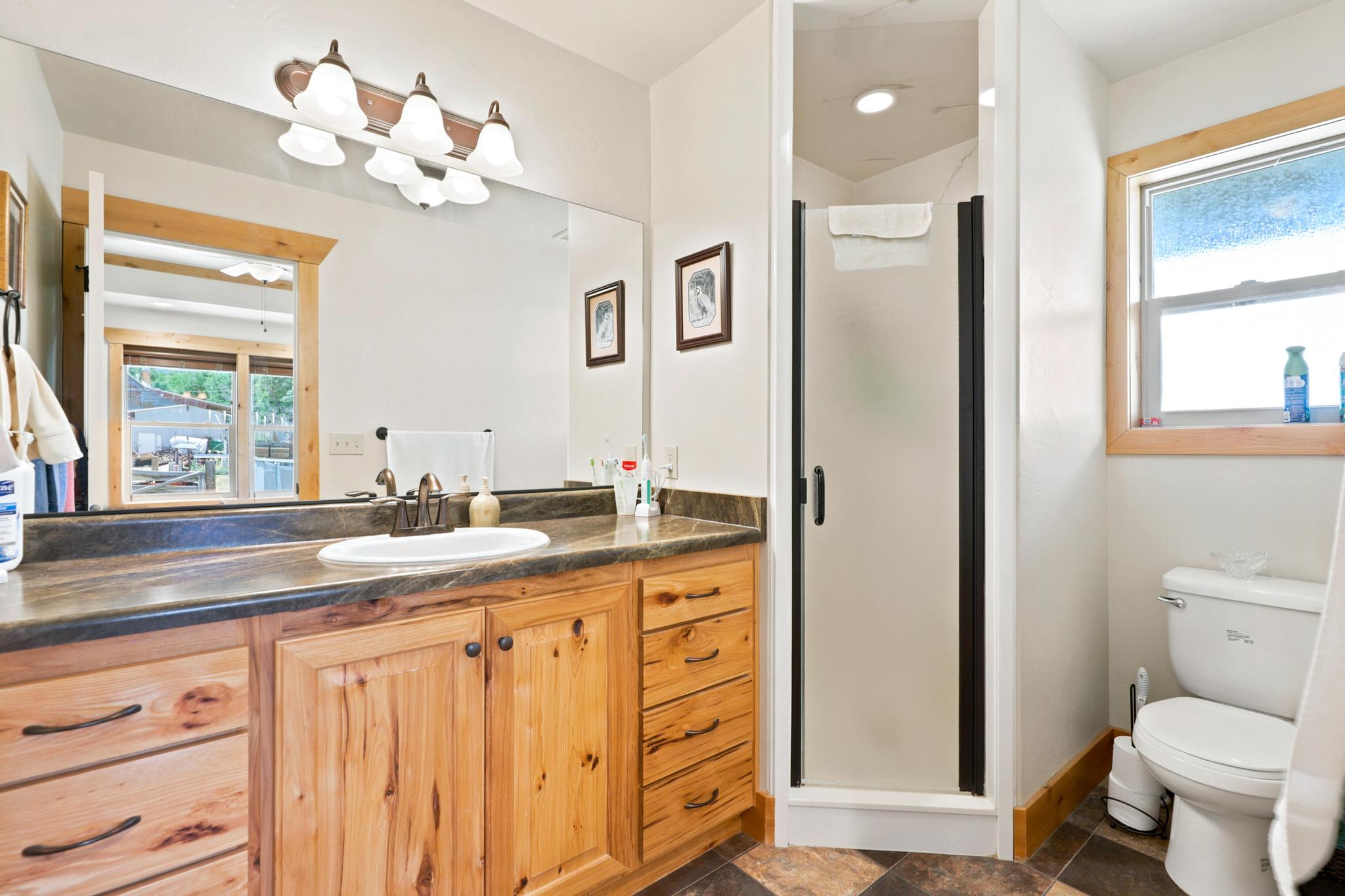 Bathroom featuring a wood-finish vanity with a single basin, dark countertop, and large mirror