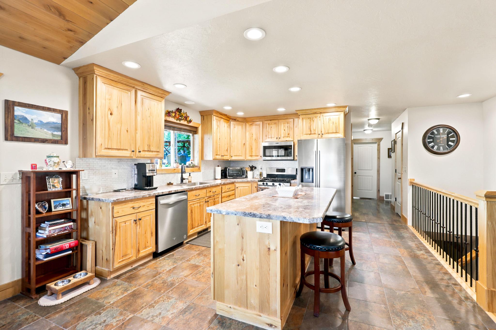 Spacious kitchen featuring natural wood cabinetry, stainless steel appliances, a multi-tone tile backsplash, and a multi-purpose island with counter seating