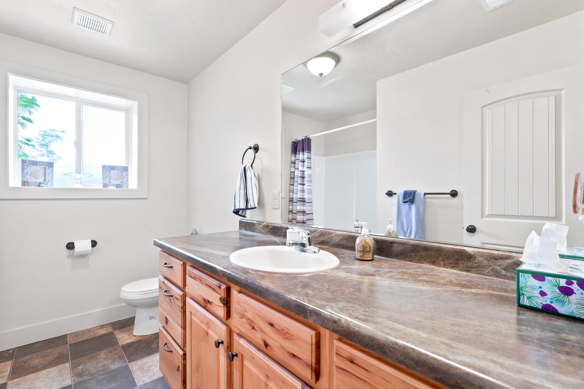 Bathroom vanity featuring a light wood-finish cabinet with dark hardware, a spacious countertop, and an integrated white sink