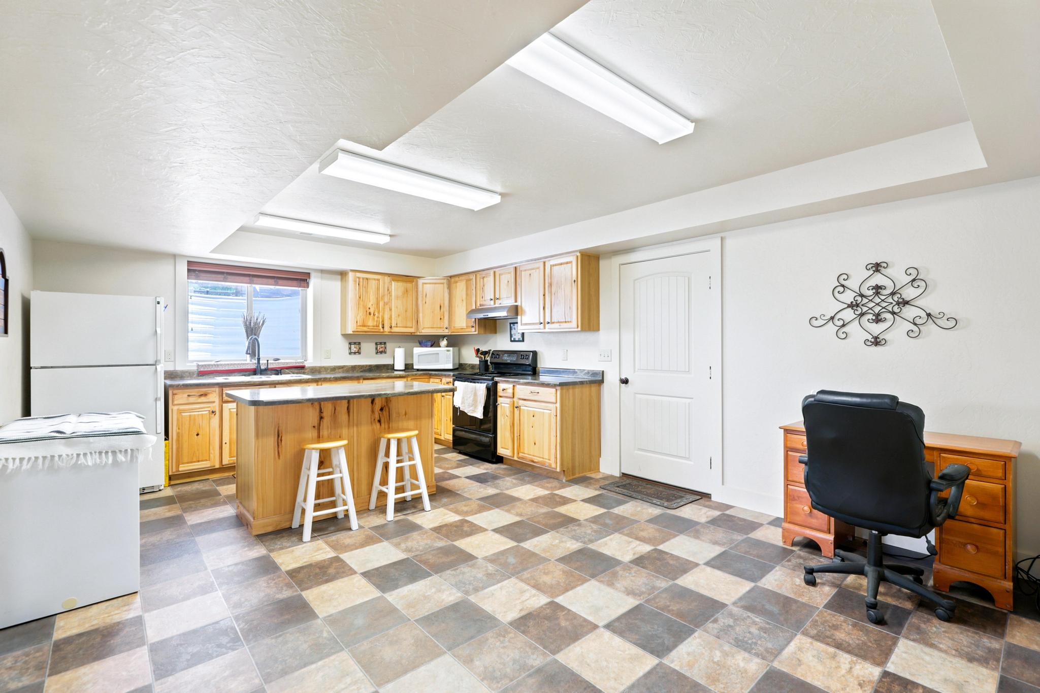 Spacious kitchen featuring natural wood cabinetry, a central island with bar seating, ample counter space, and durable checkerboard-patterned flooring