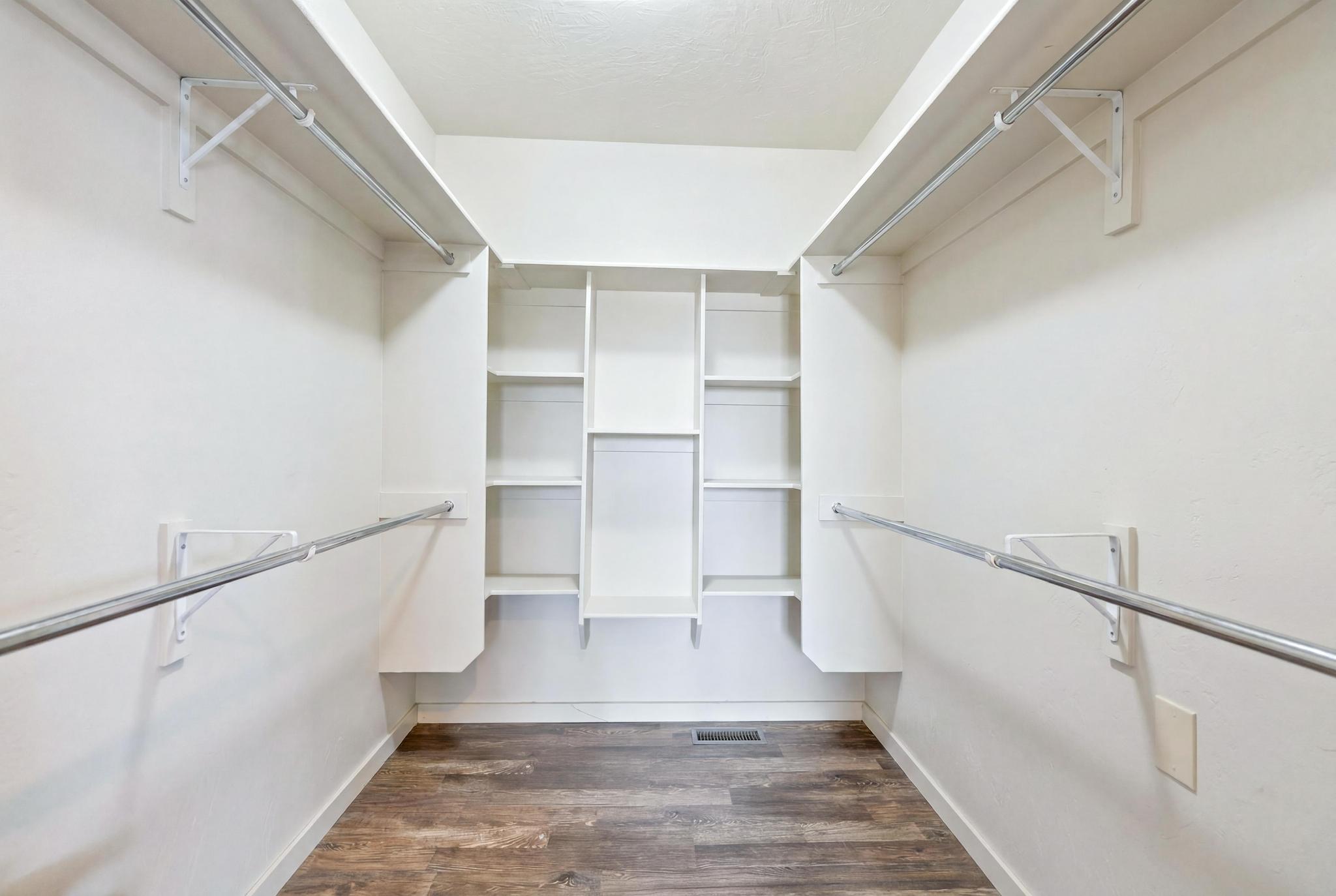 Spacious walk-in closet featuring white built-in shelving, dual chrome hanging rods, and wood-finish flooring