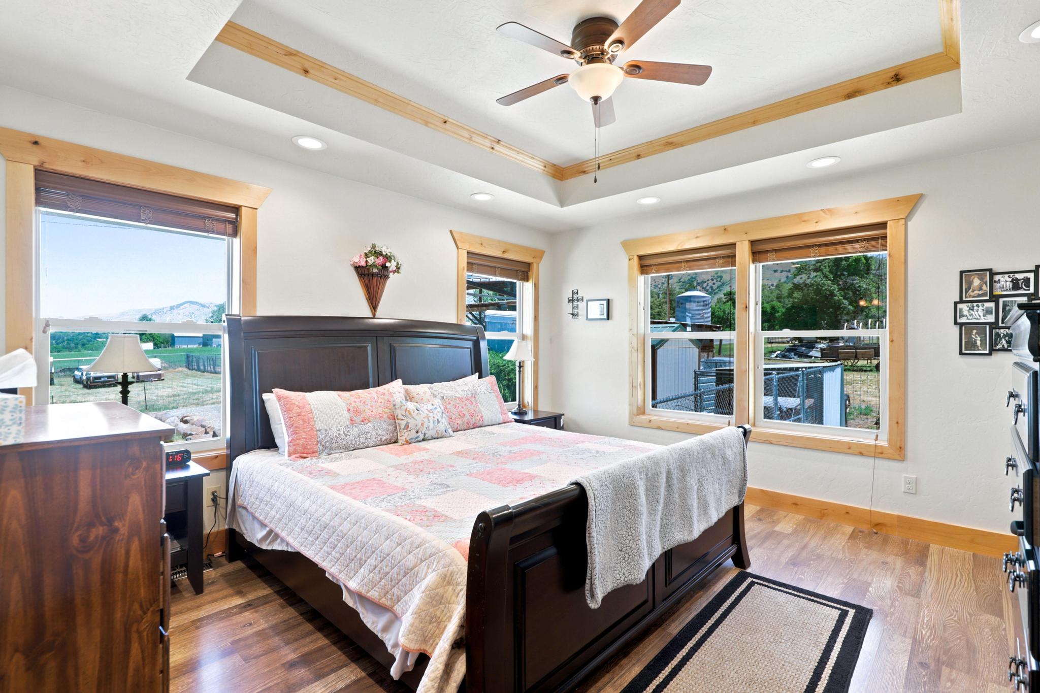 Spacious room featuring wood-finish flooring, a tray ceiling with wood trim, and a ceiling fan