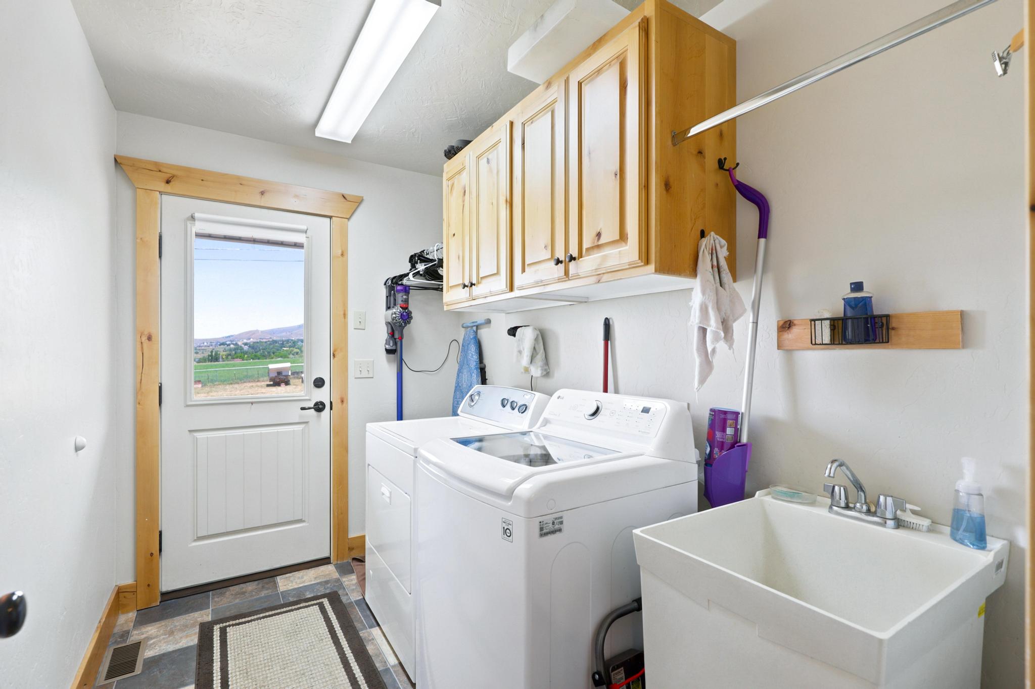 Laundry area featuring wood-finish cabinetry, a utility sink, and durable tile flooring