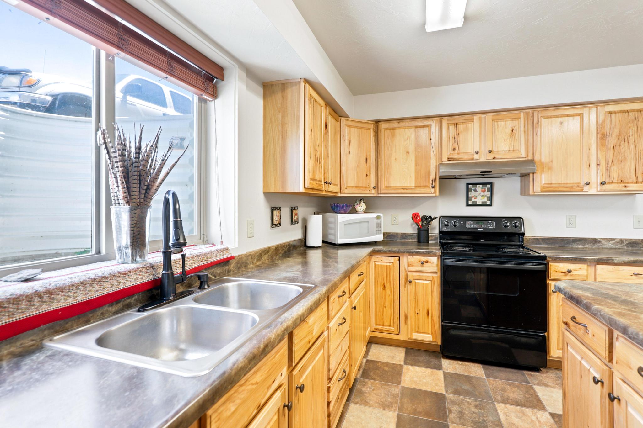 Kitchen featuring natural wood cabinetry, a dual-basin stainless steel sink with a matte black faucet, and patterned floor tiling