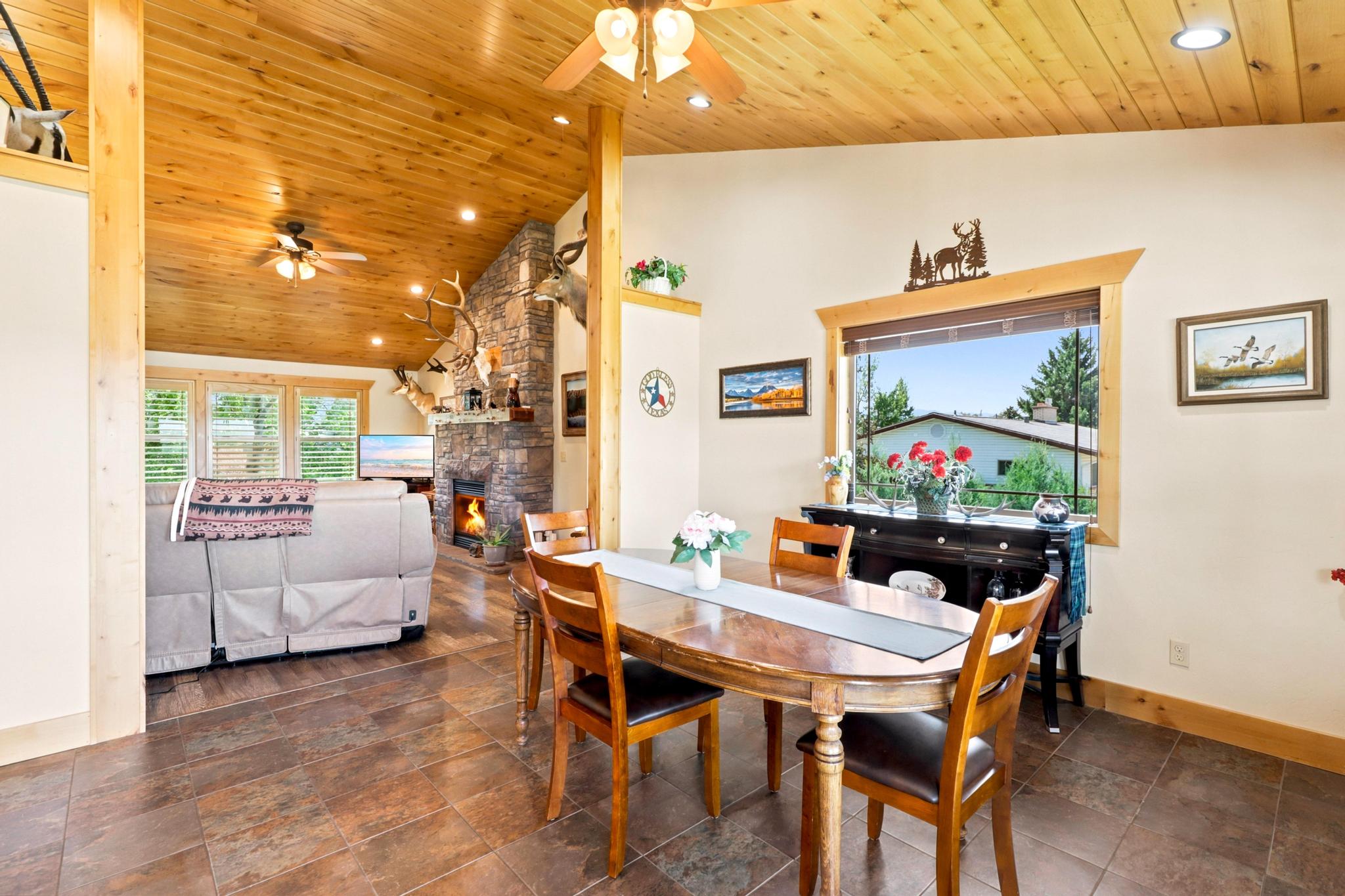 Dining area featuring a wood-finish oval table and chairs, adjacent to a living area with a stone-clad fireplace