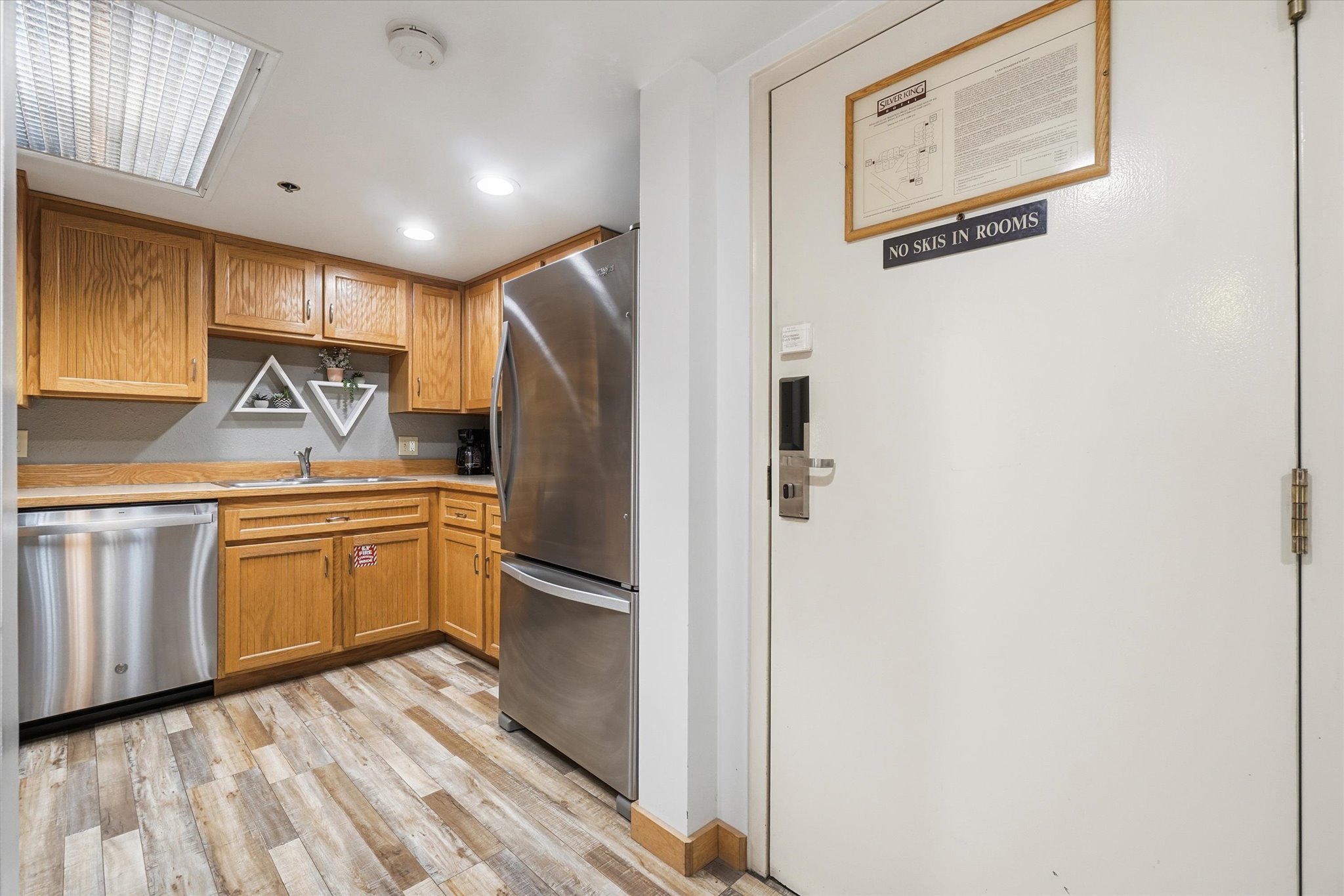 Kitchenette featuring wood-finish flooring, stainless steel appliances, wood cabinetry, and a single basin sink