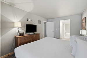 Spacious bedroom featuring light grey walls, carpet flooring, a built-in wall vent, and a hallway leading to an additional room with a built-in bathtub