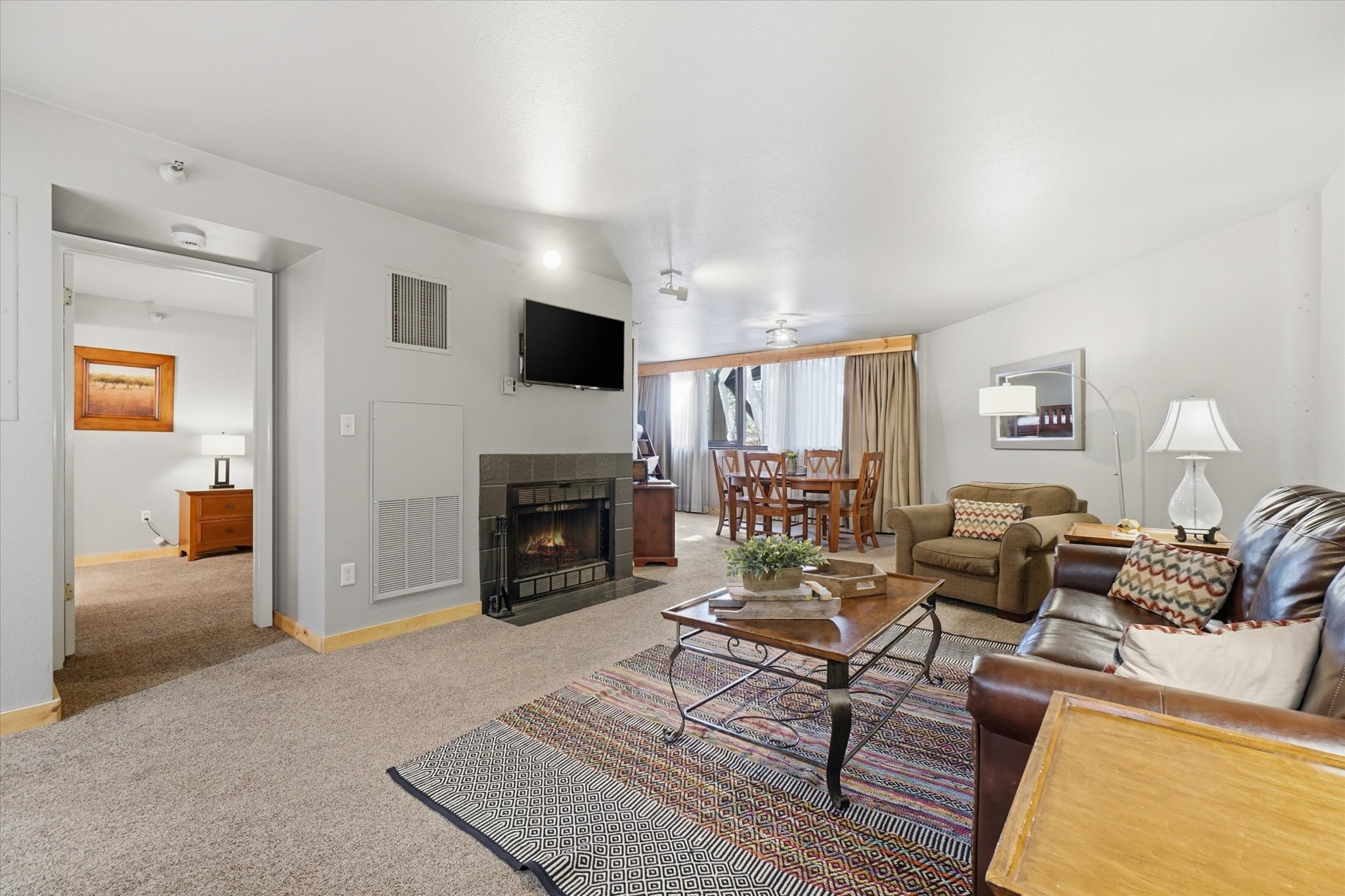 Living room featuring a fireplace with a dark tile surround, wall-mounted television, and carpet flooring