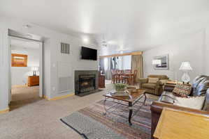 Living room featuring a fireplace with a dark tile surround, wall-mounted television, and carpet flooring